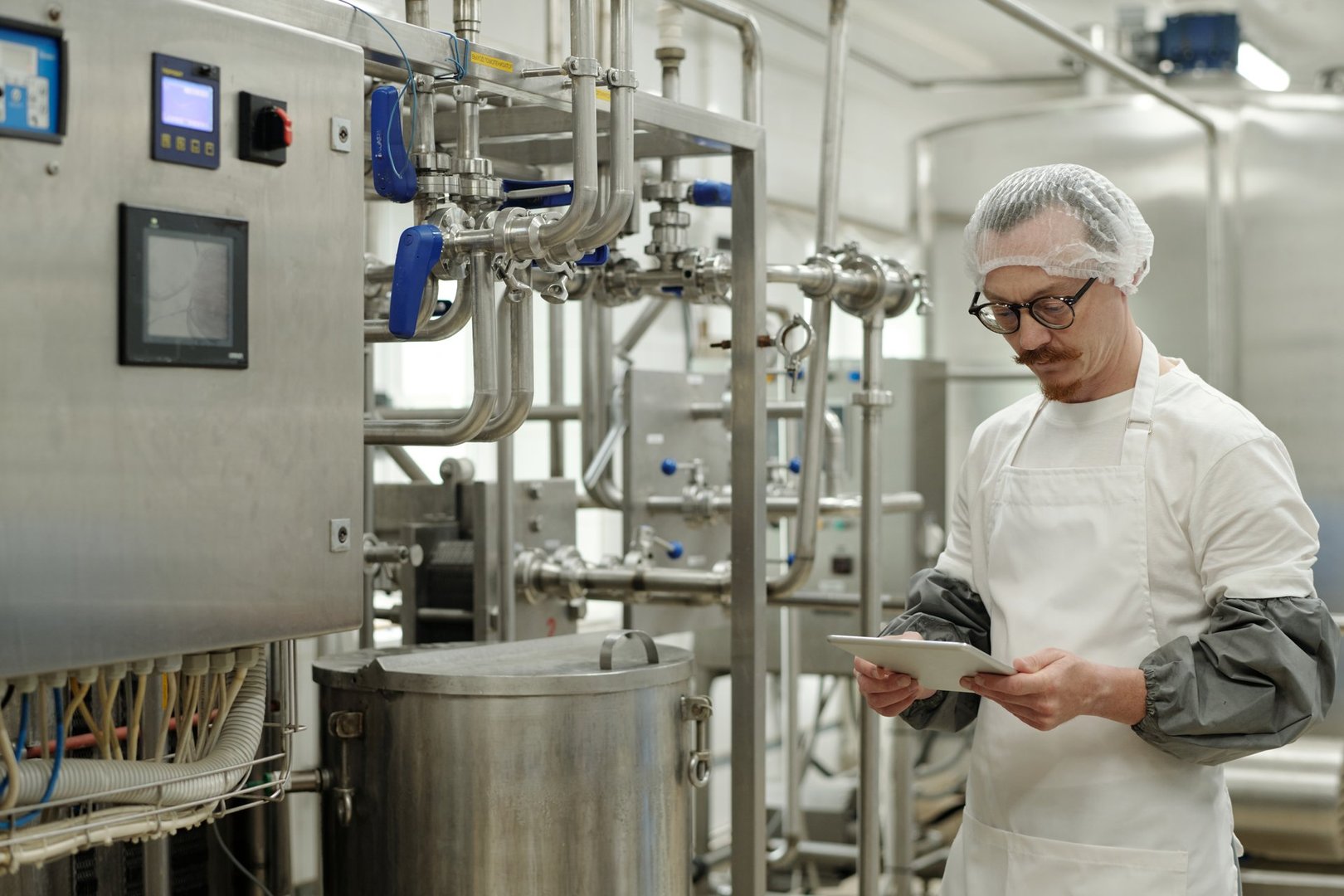 Male worker using tablet while overseeing food processing equipment in a modern facility operating machinery