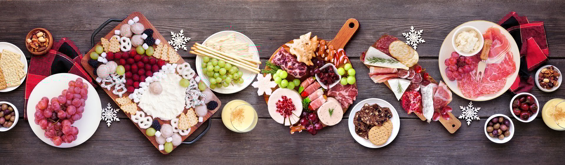 Christmas holiday charcuterie table scene on a dark wood banner background. Top down view. Variety of cheese, fruit and meat appetizers.