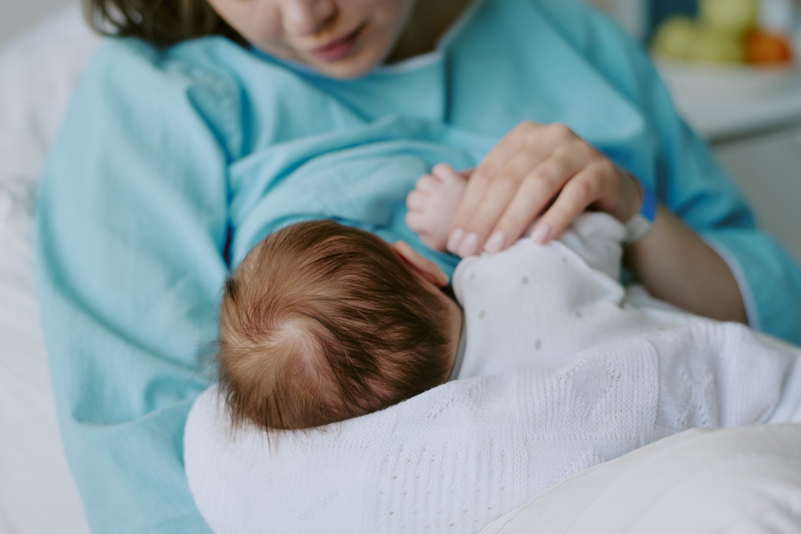 Mother breastfeeding newborn baby in hospital room while holding child gently in arms. Background features hospital equipment and soft focus items creating serene atmosphere