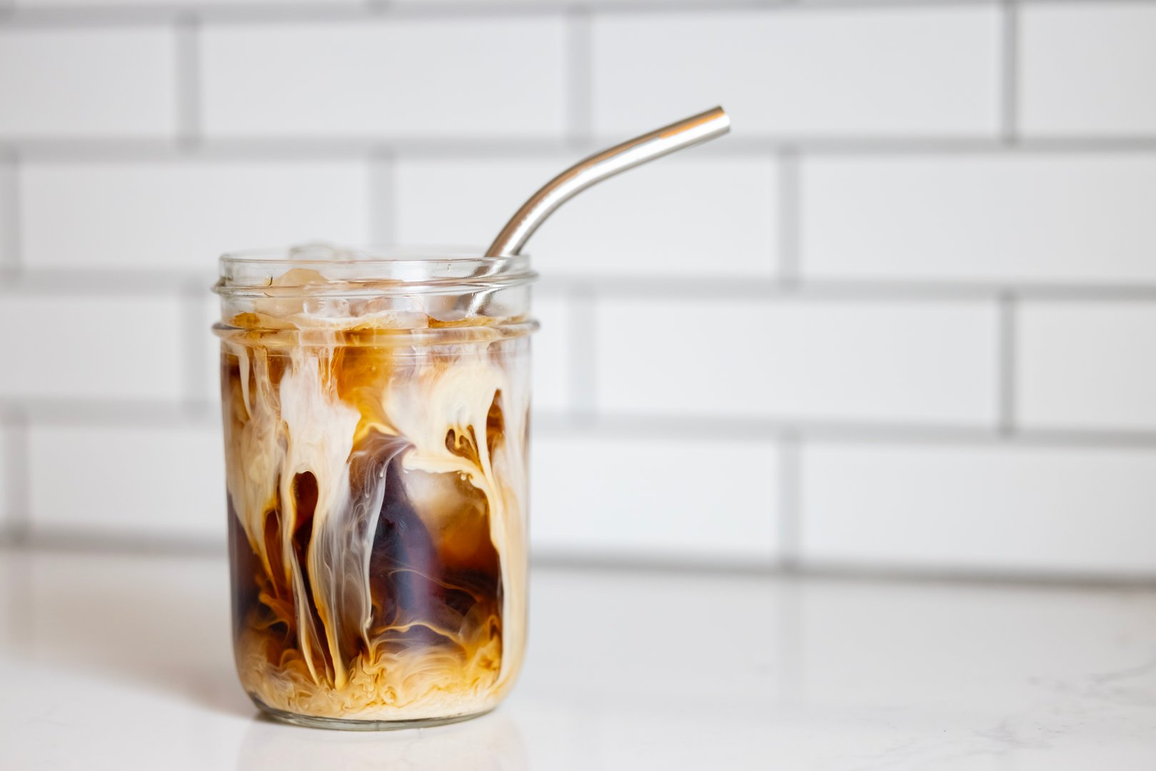 A Glass of Homemade Cold Brew Coffee and Cream with a Stainless Steel Straw Resting on a White background