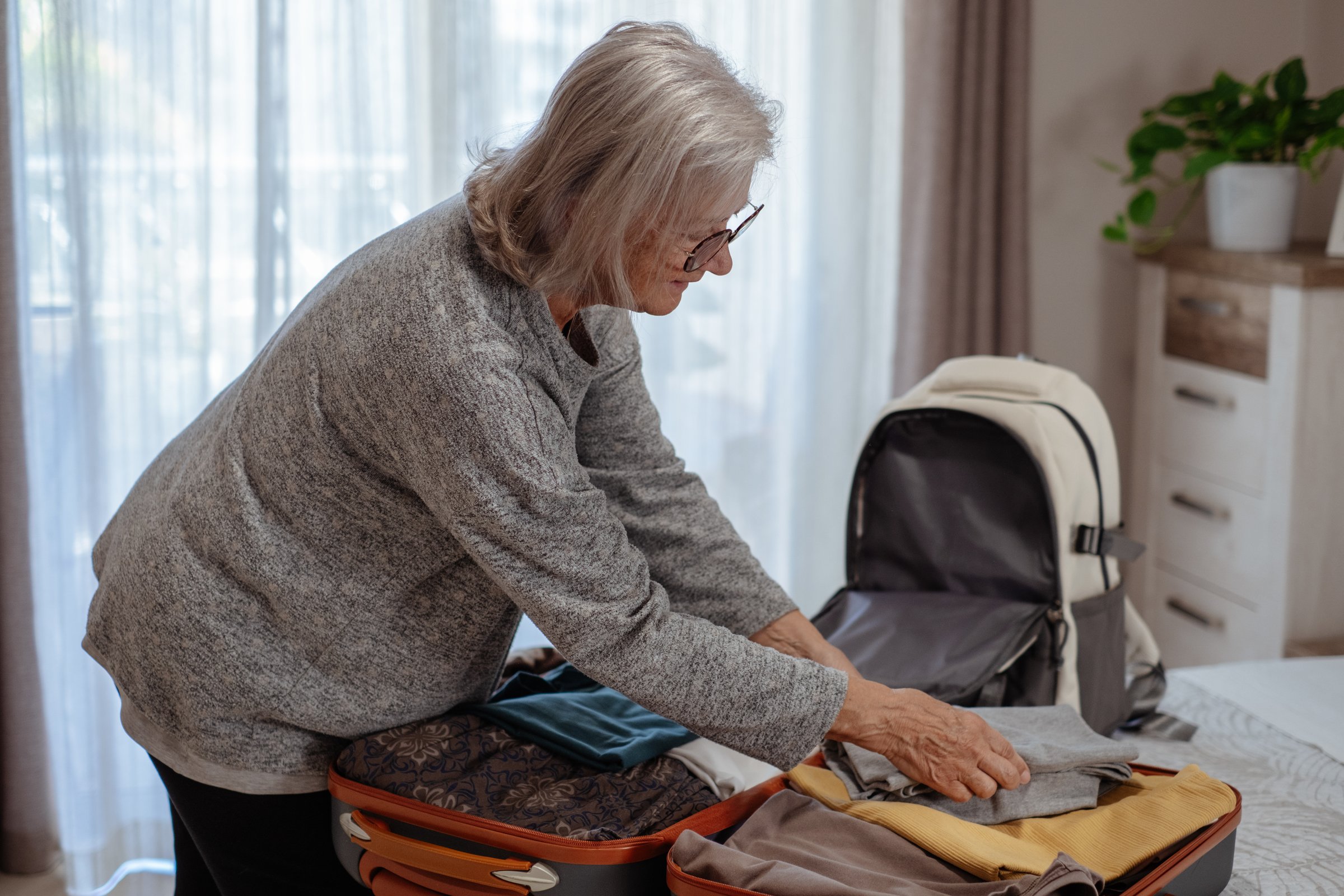 Full suitcase concept, elderly woman packing, preparing luggage case and backpack for weekend or journey, luggage of clothes, travel trip