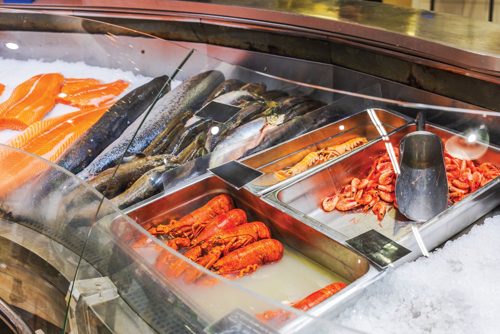 Fresh seafood display with salmon, fish, lobsters, and shrimp on ice in grocery store seafood section. Sweden.