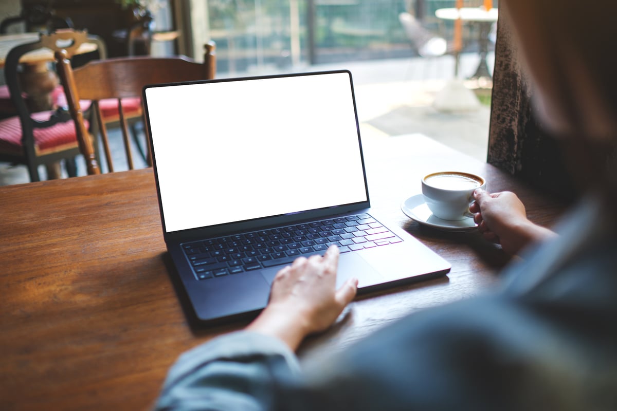 Mockup image of a woman working on laptop computer with blank white desktop screen while drinking coffee in cafe
