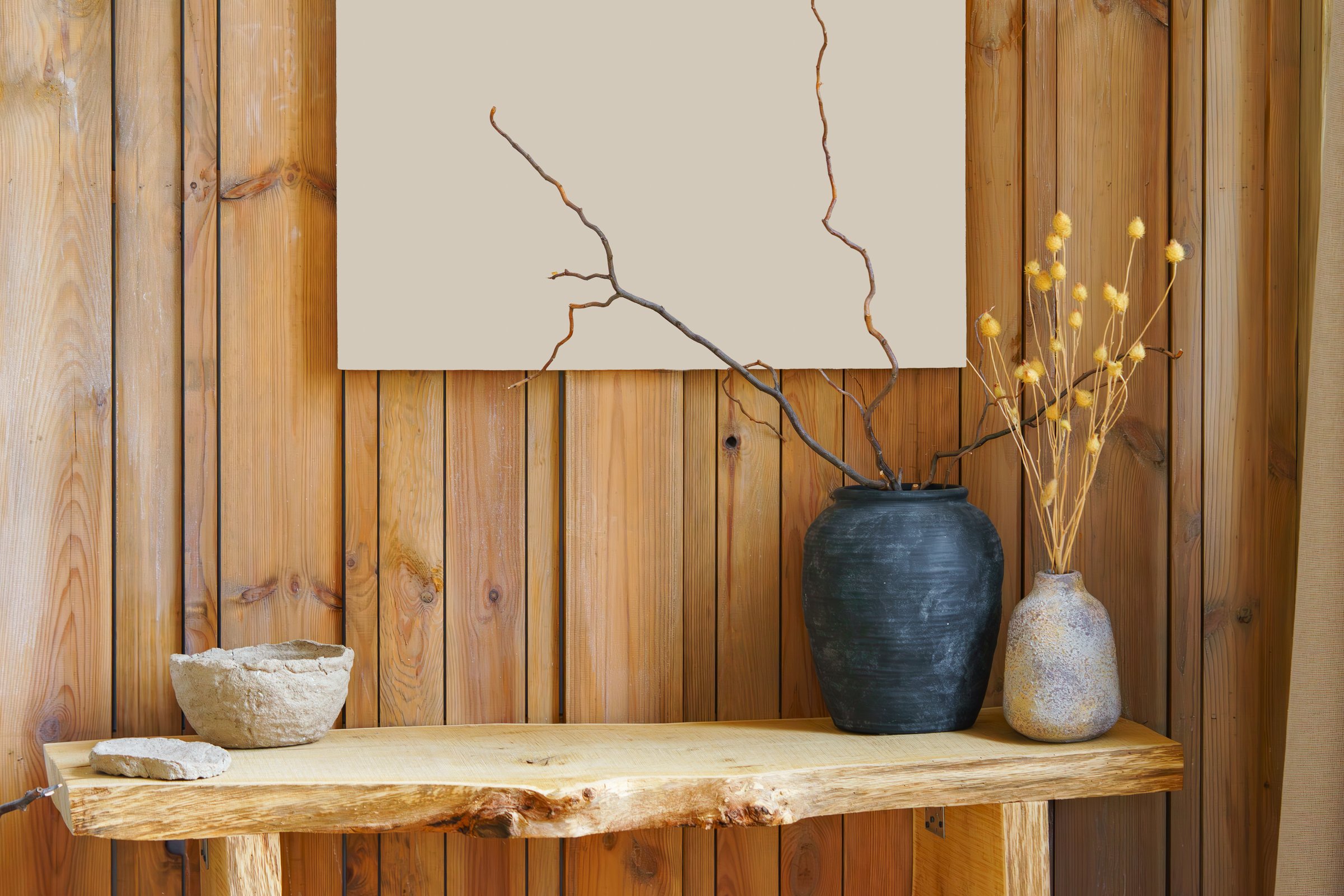 Simple handmade pottery and dried branches on wooden shelf on rustic wooden wall background. Natural light highlights warm textures creating cozy minimal interior composition for calm home mood.