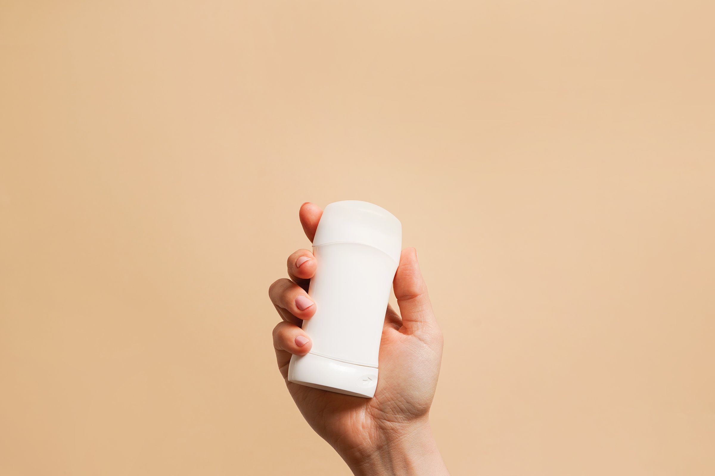Hand holding antiperspirant, white deodorant on beige background, copy space