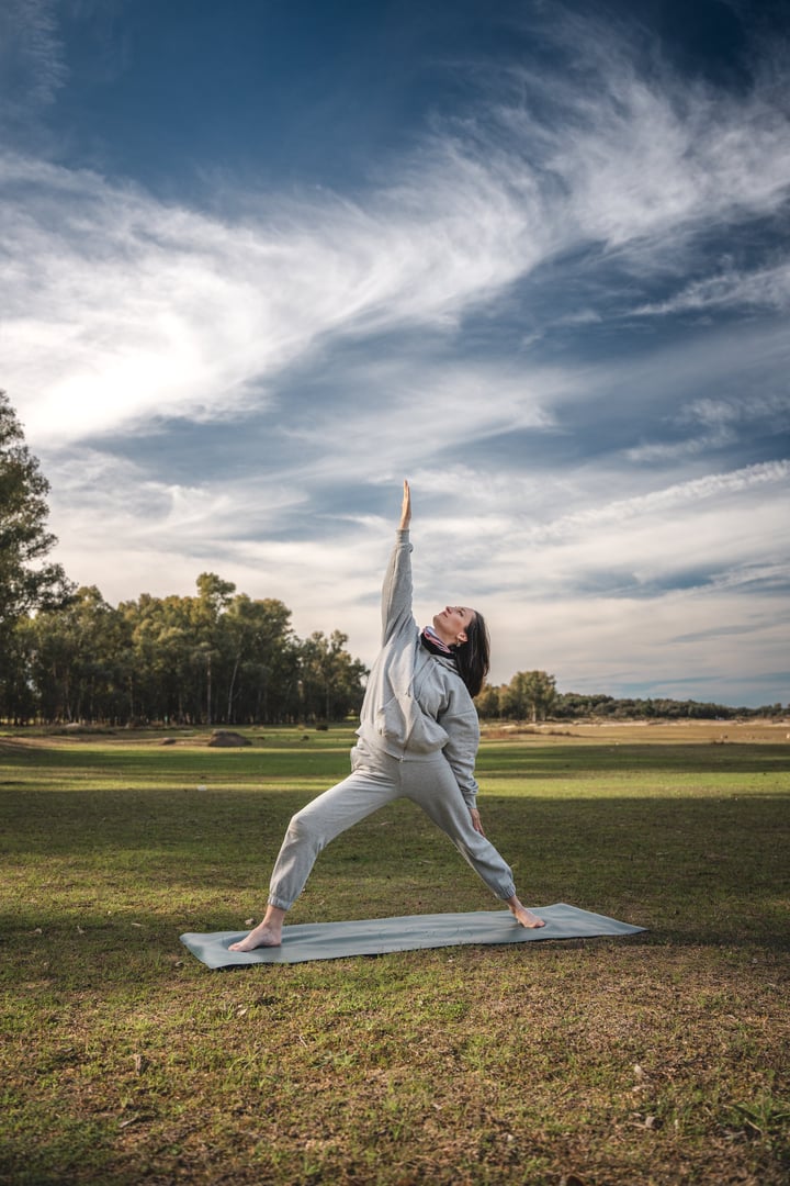 A woman is doing yoga in a field with a blue mat. The sky is cloudy and the grass is green