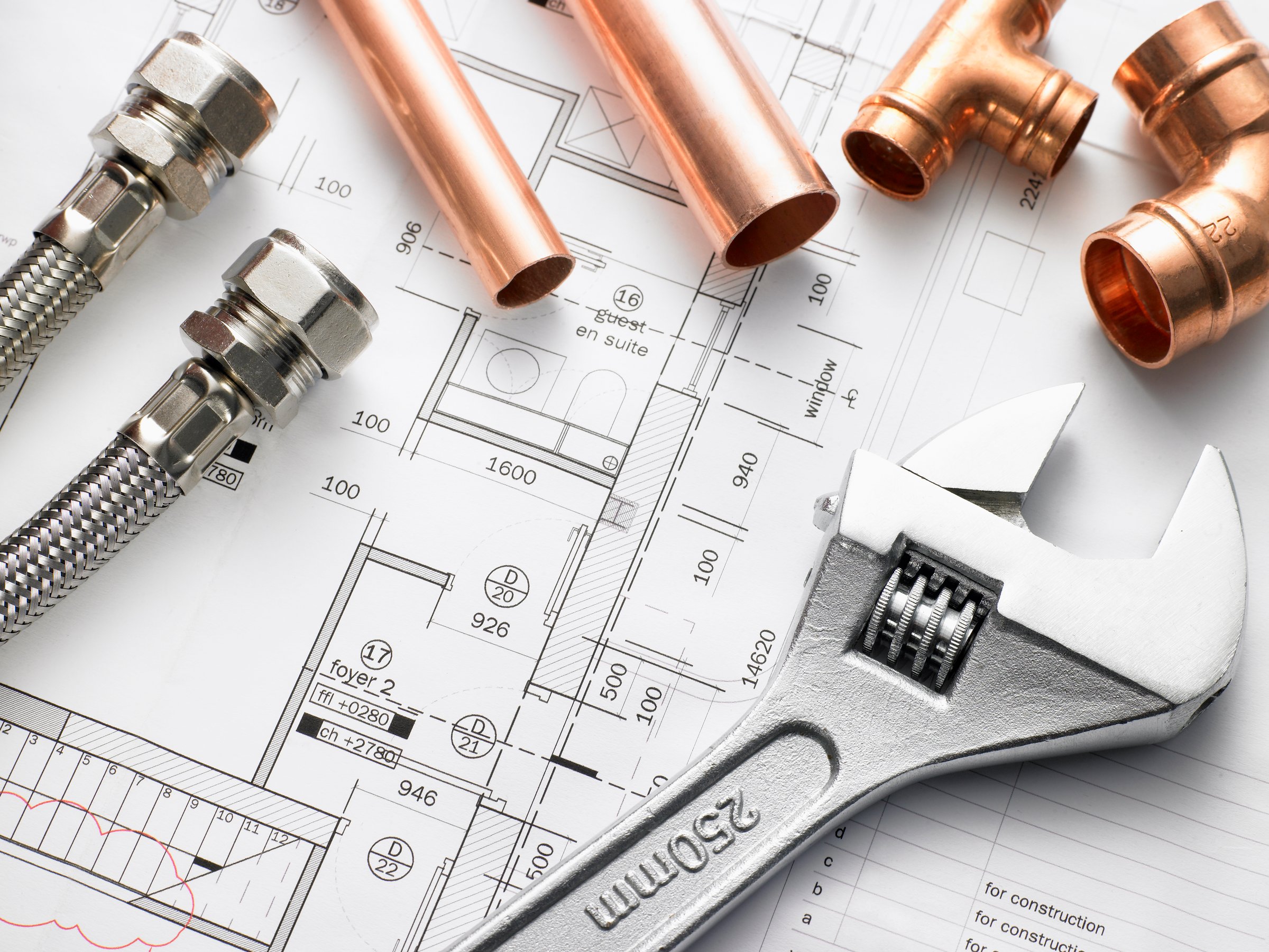 Plumbing tools and copper pipes on a blueprint, featuring a wrench and flex hoses, suggesting planning or installation work.