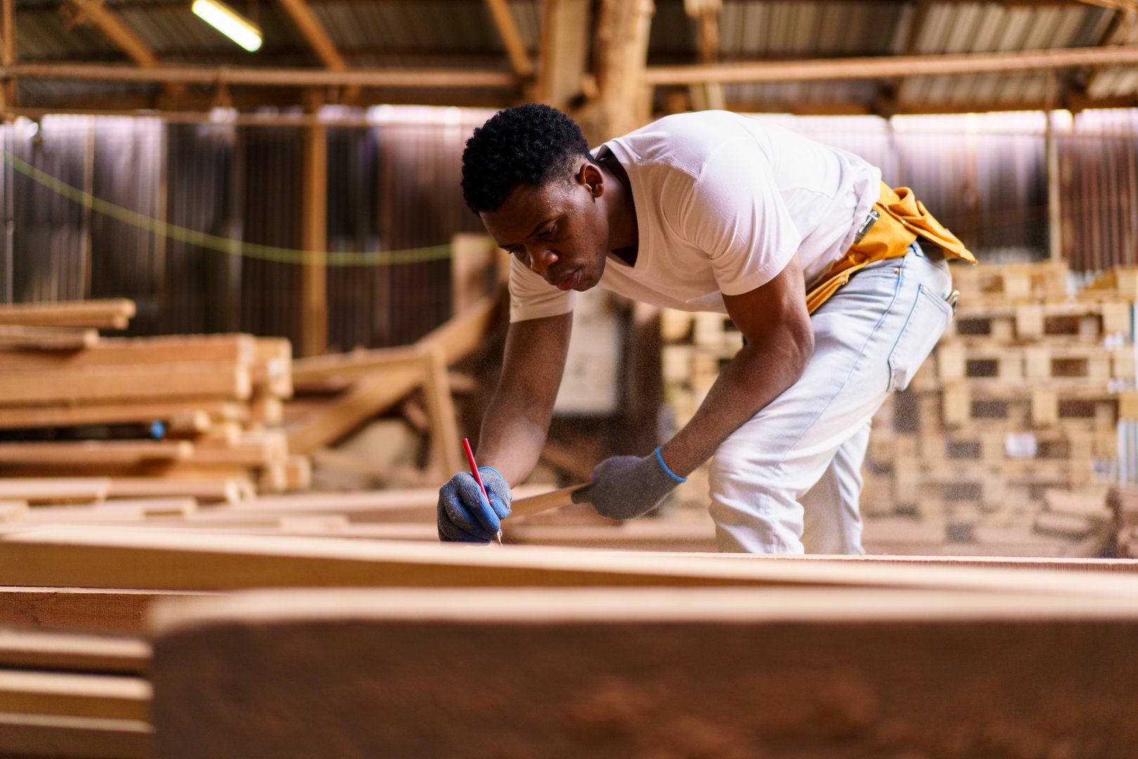 An African carpenter in a woodworking workshop carefully inspecting a sawn wooden plank with focus and precision. Represents craftsmanship, manual labor, skill, industry, craftsmanship and profession.