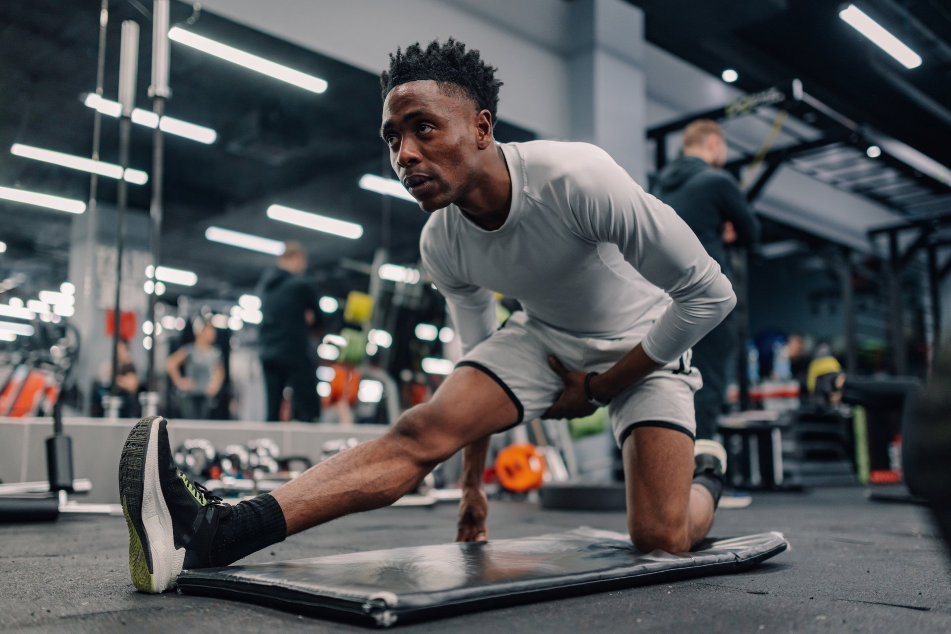 Focused young athlete stretching legs on mat in modern gym, preparing for intense workout session