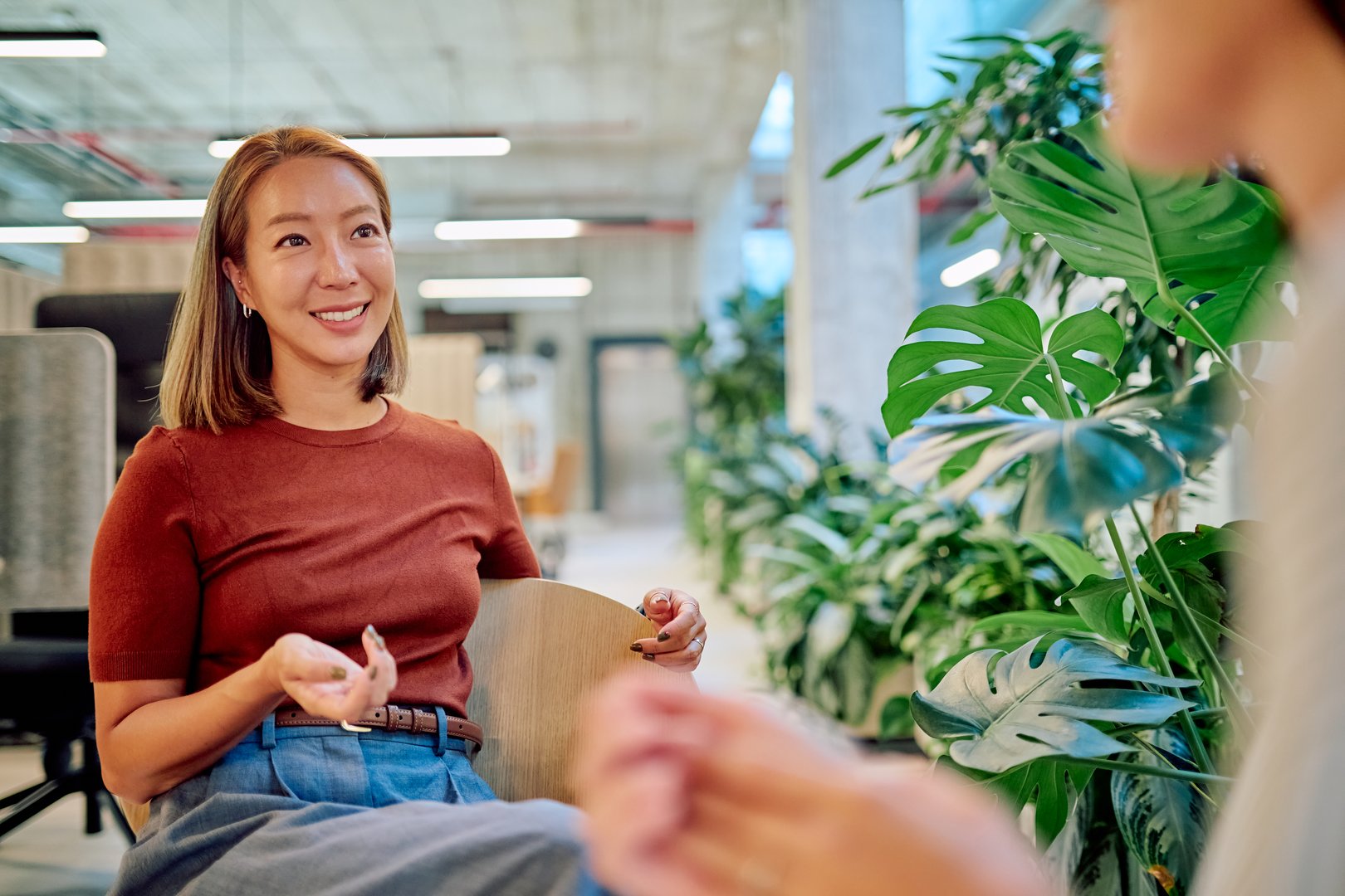 Asian businesswoman gesturing while discussing with colleague in a modern green office with many plants