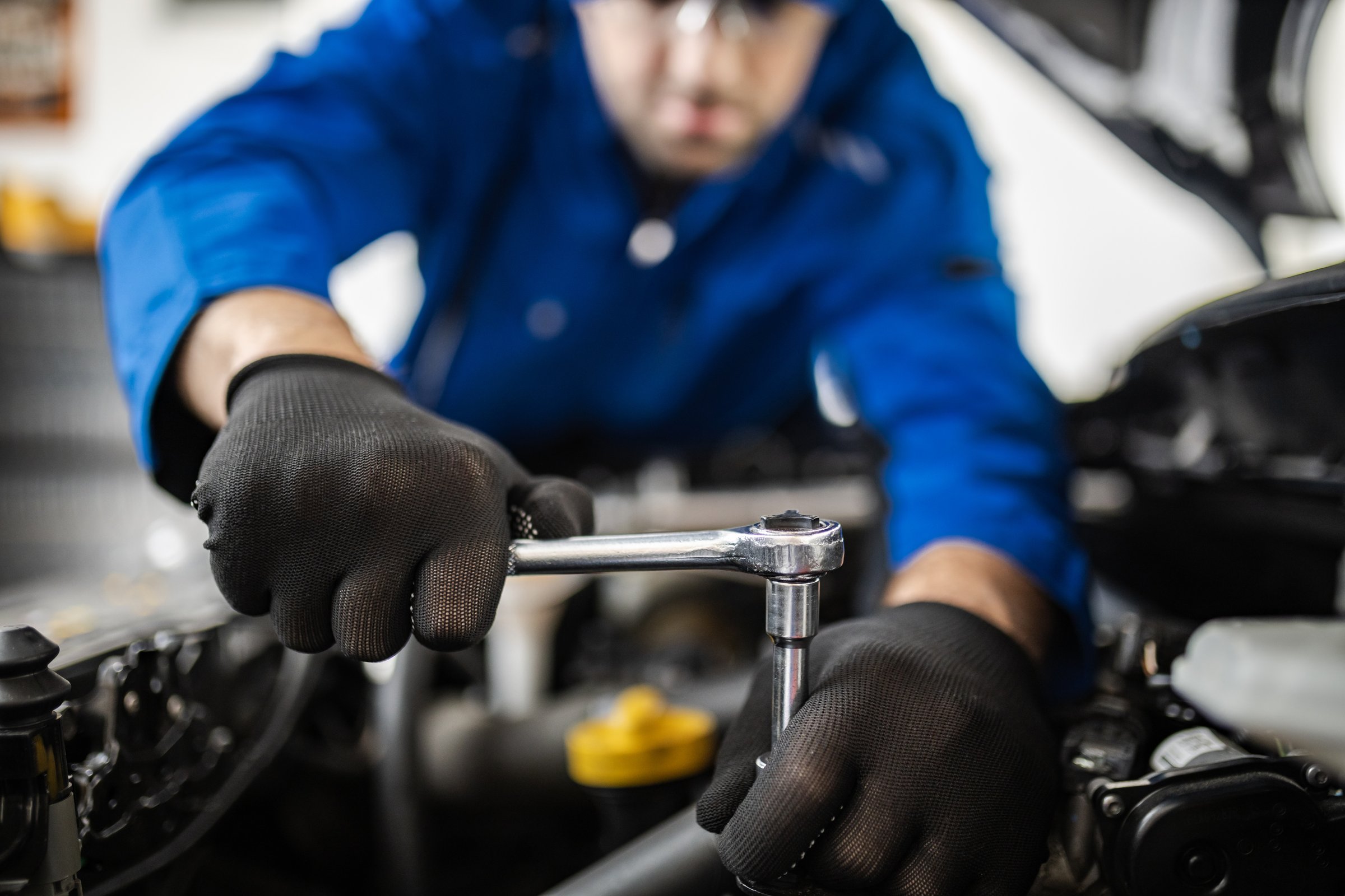 A skilled mechanic focuses intently on fixing a car engine, utilizing a ratchet tool with gloved hands in a bright and organized workshop space.