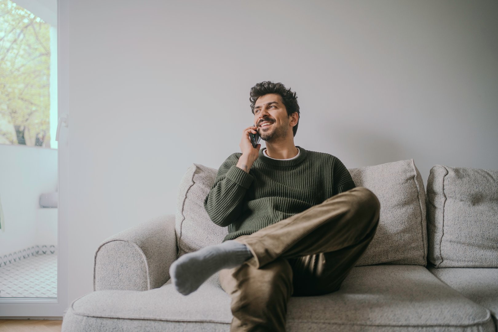 Thoughtful Young Handsome middle eastern man sitting on the couch and talking on his phone