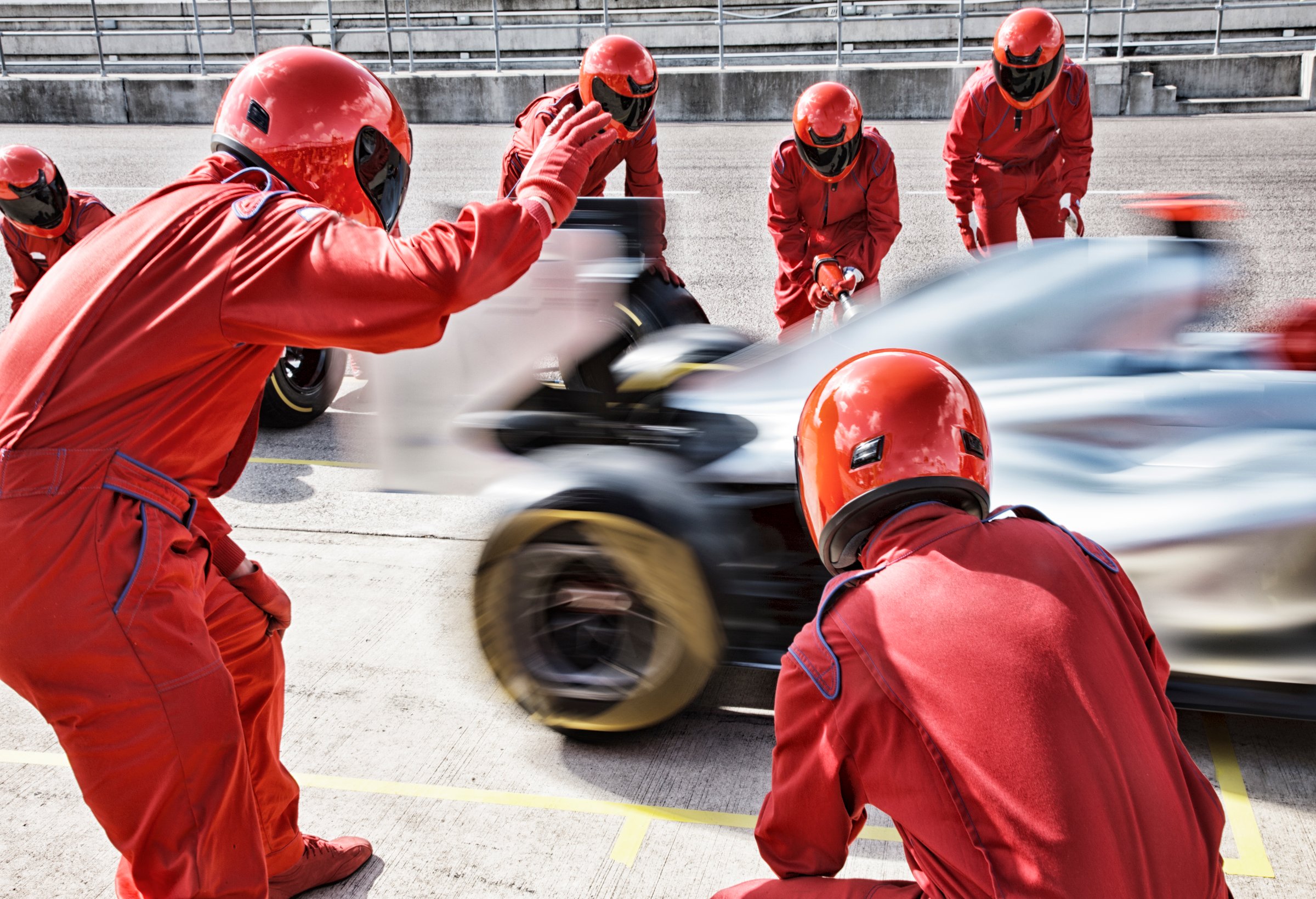 Pit crew in red uniforms working on a speeding Formula 1 car during a pit stop at a race track.
