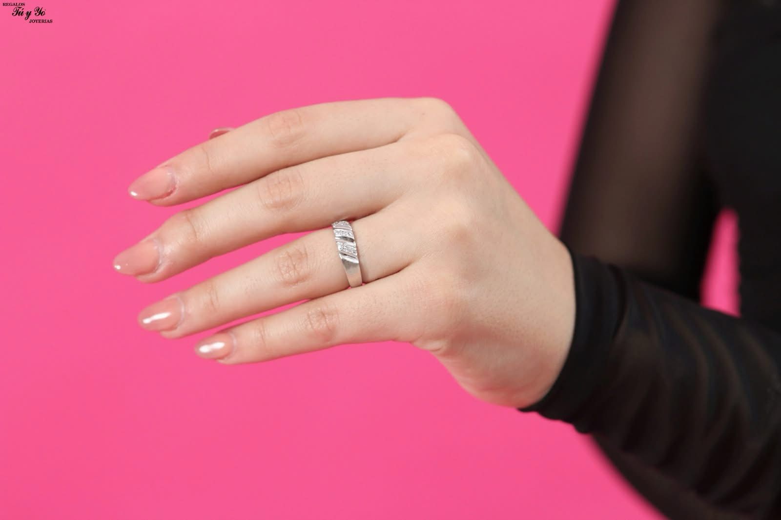 Close-up of a hand wearing a silver ring with small diamonds against a pink background.