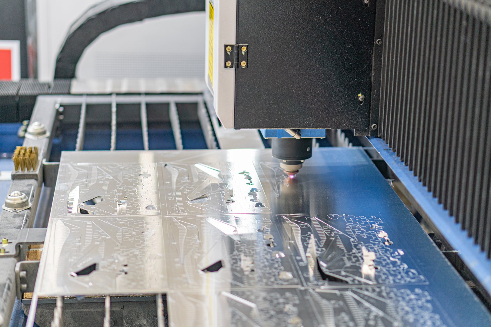 Close-up view of an industrial laser machine in operation, processing a rectangular object with multiple smaller components Background consists of mechanical parts and structures typical of industri