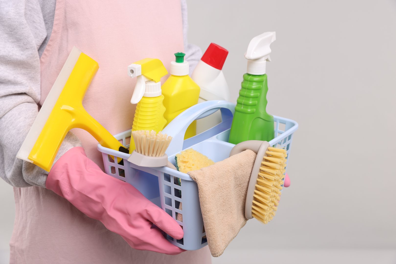 Woman with basket of cleaning supplies on light background, closeup
