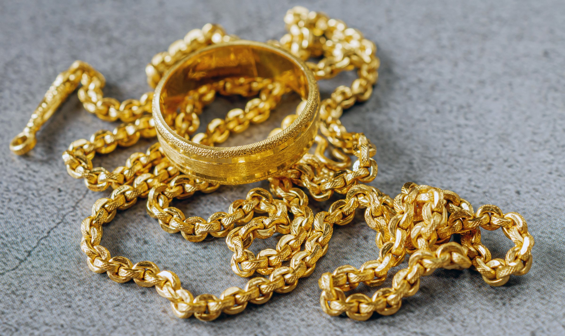 Gold price, gold jewelry, close-up of gold ring and gold necklace on grey background.