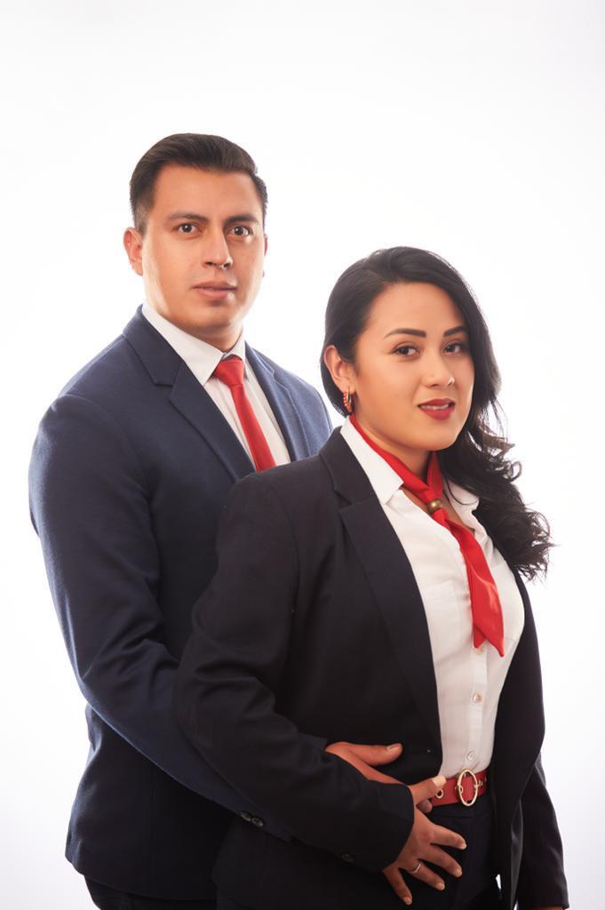 Two people in formal attire, both wearing navy suits and red ties, standing together with a white background.
