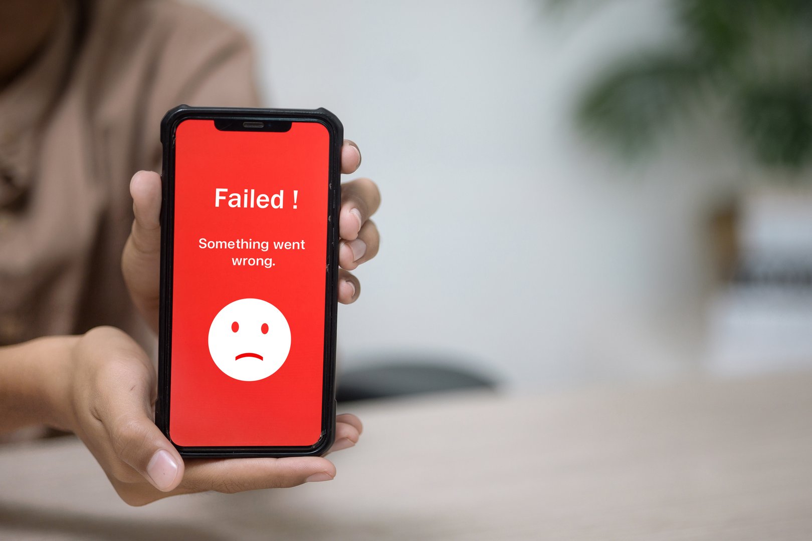 Hand holding a phone displaying a red screen with Failed! Something went wrong and sad emoji, indicating transaction failure, system error, or issue notification.