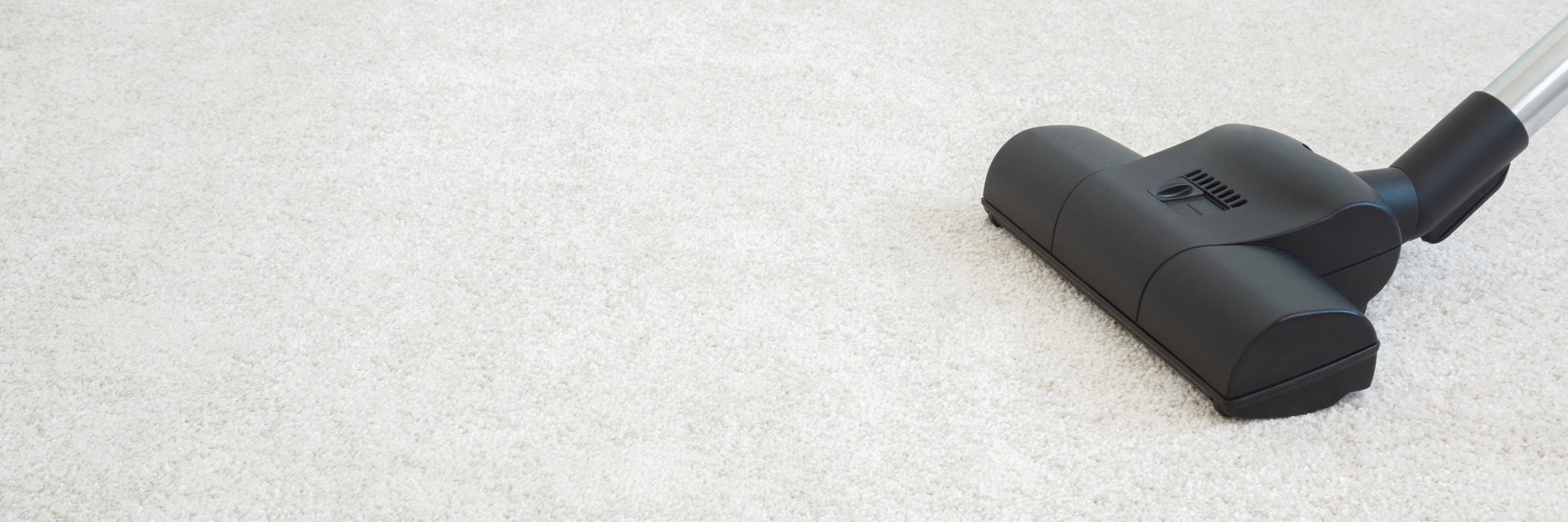 Dark black vacuum cleaner nozzle on white home carpet background. Closeup. Side view. Wide banner. Empty place for text.