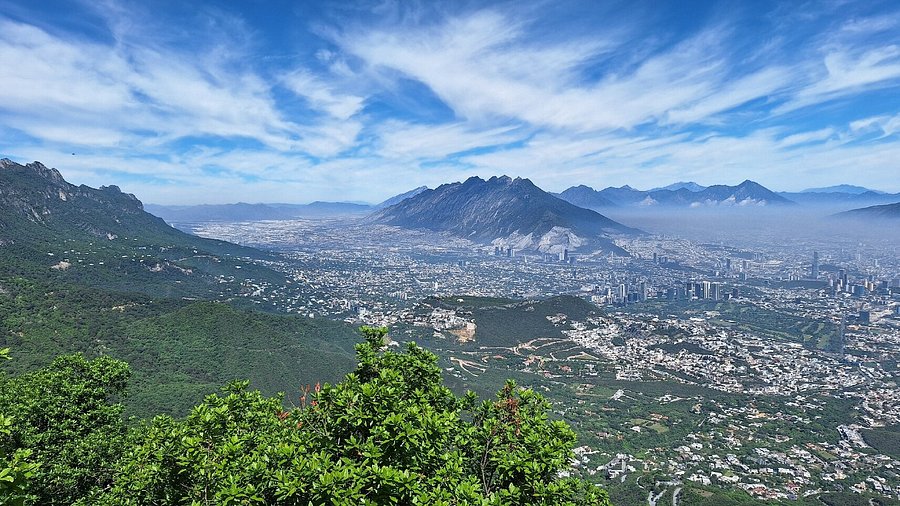 Aerial view of a city surrounded by mountains under a blue sky with wispy clouds.
