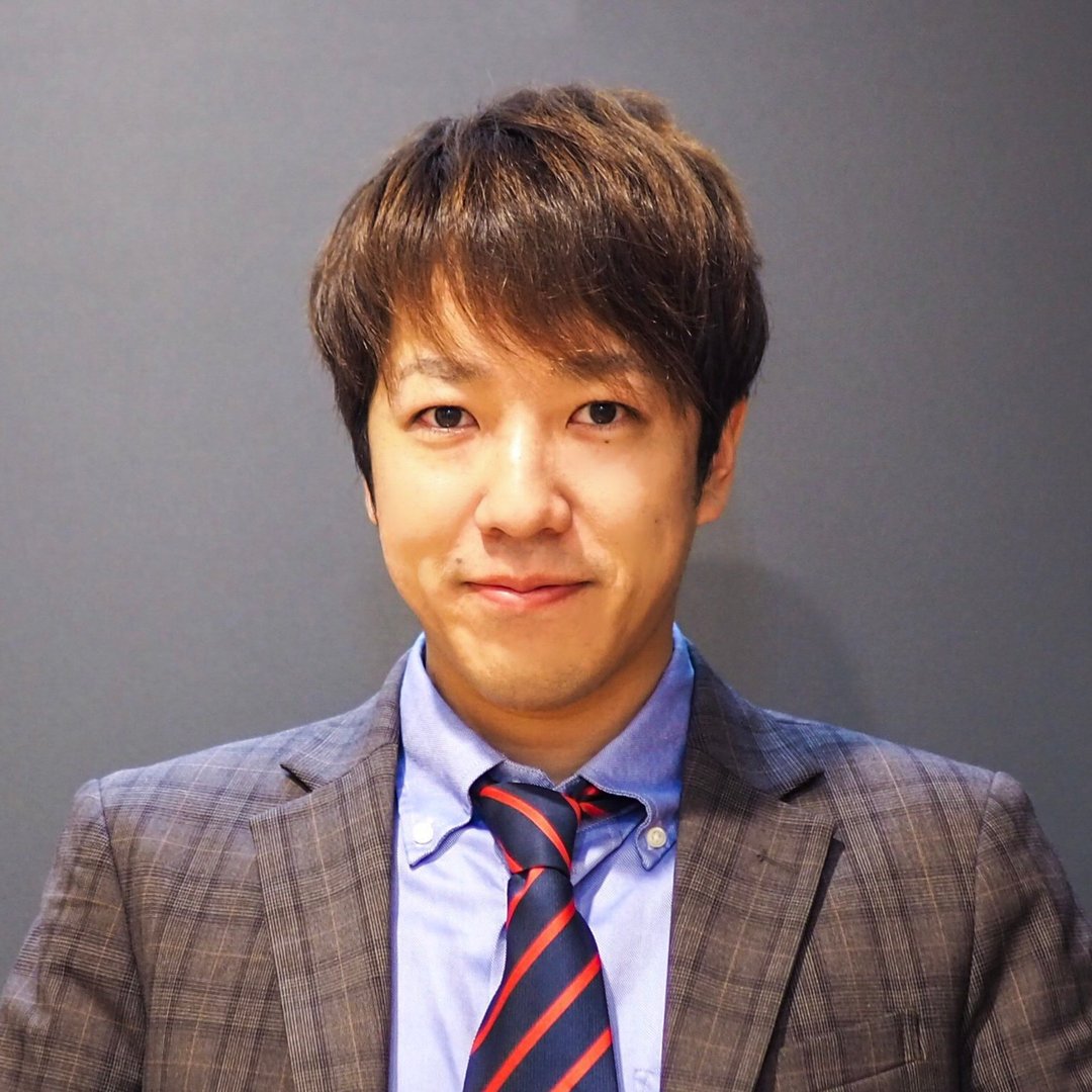 Portrait of a person wearing a checkered suit, blue shirt, and striped tie, smiling against a plain background.