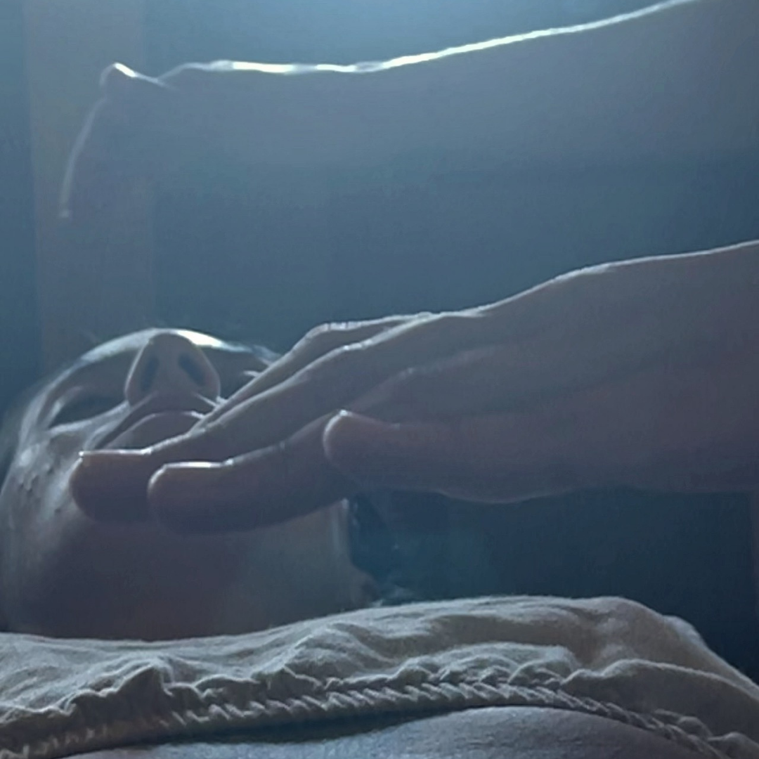 A person lying down with another person's hands hovering above, possibly performing energy therapy or healing.
