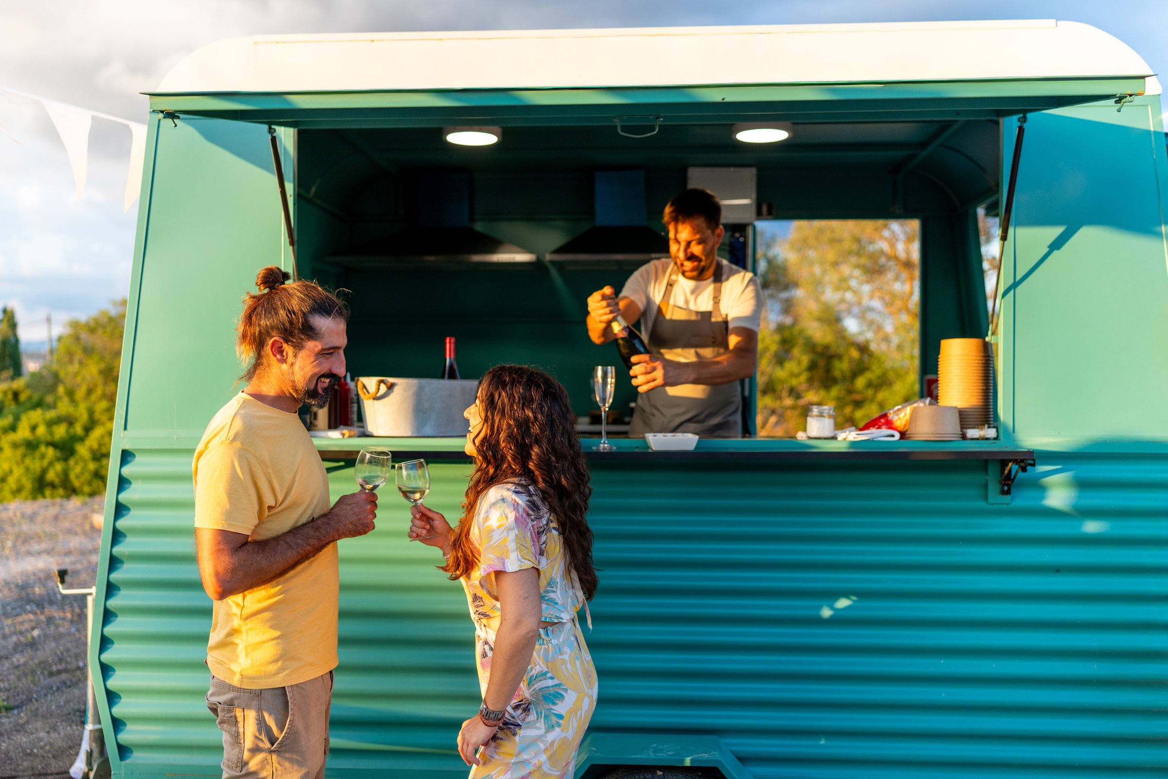 Friends cheering with wine glasses at a food truck during an outdoor celebration