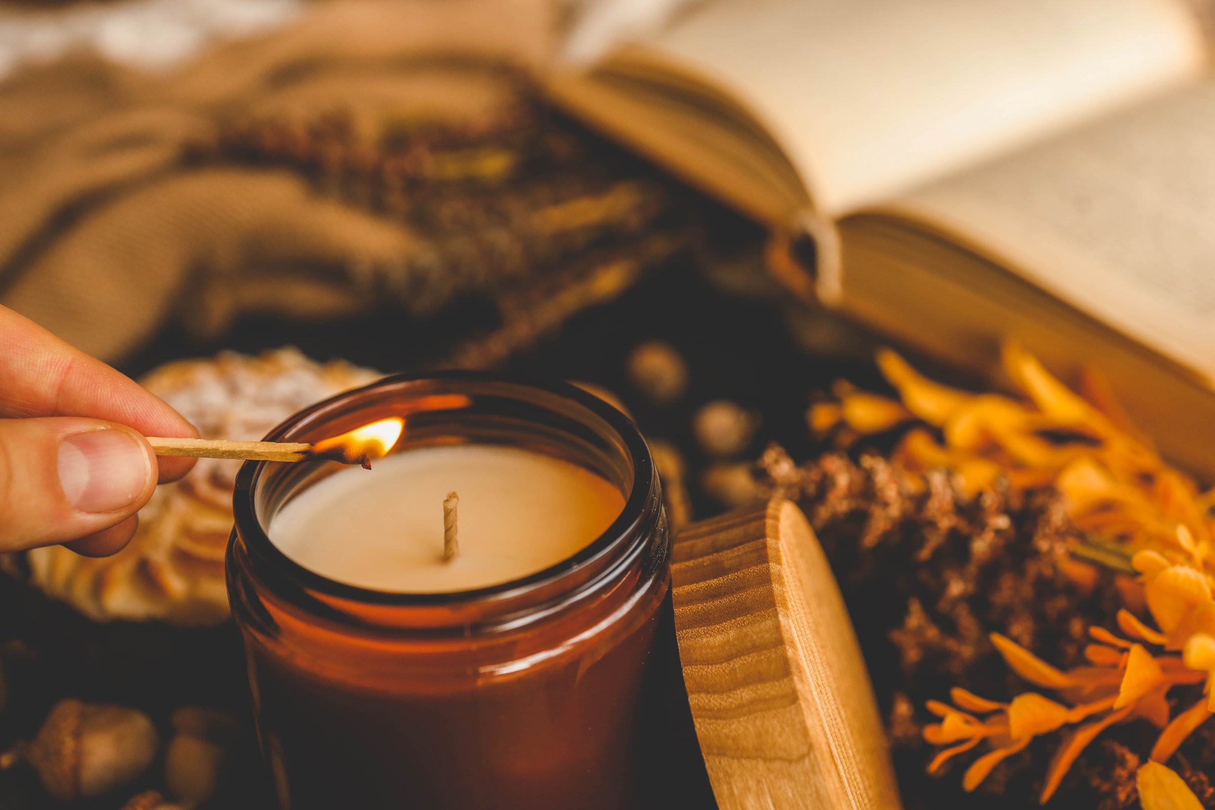Close-up of a person lighting a scented candle with a matchstick, creating a warm and cozy ambiance, perfect for a relaxing evening.