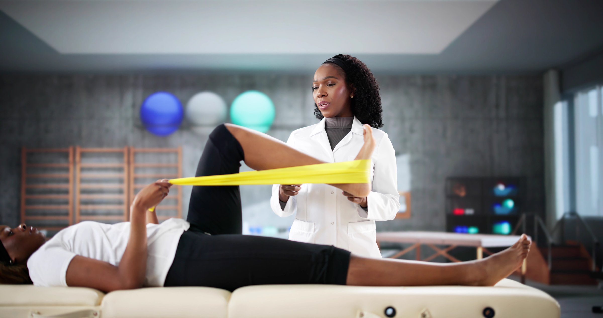 Physio treating young Black woman's knee injury in clinic session.