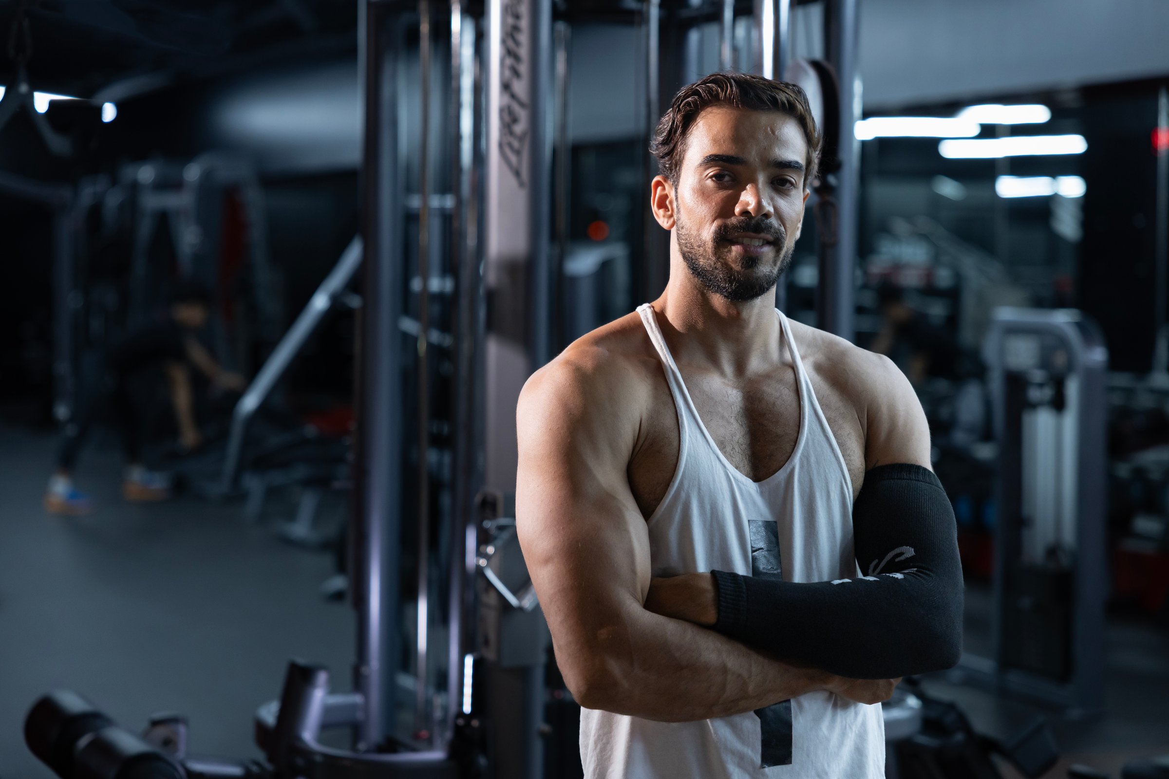 Portrait of caucasian muscular man with perfect abs and bicep muscle inside gym with dark background for exercise and workout in high contrast low key lighting studio