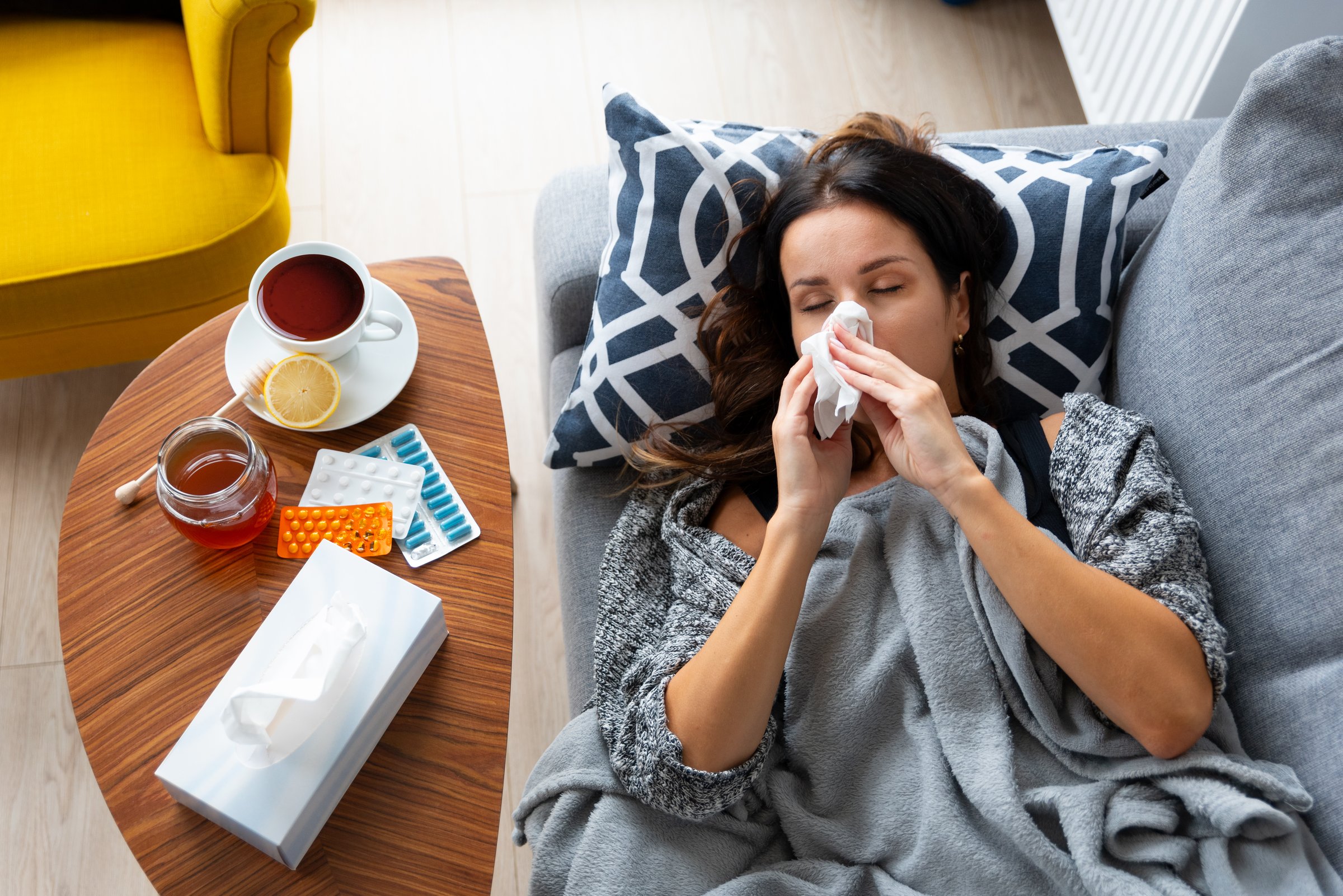 Woman is laying on a couch with a tissue in her mouth. A cup of tea is on a table next to her
