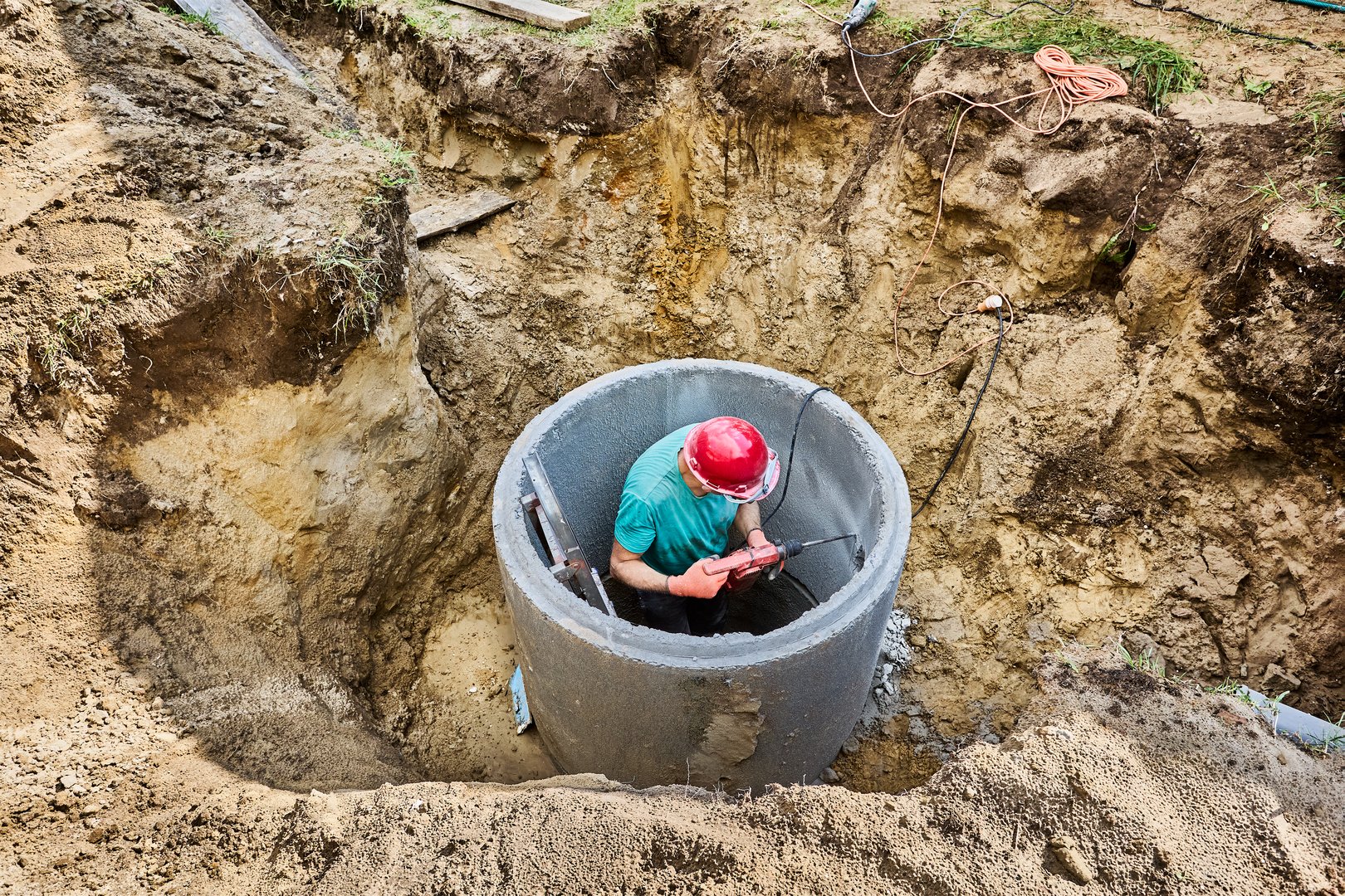 Septic tank builder crushes  wall of concrete ring with drill with cord during installation of an autonomous sewage system in private country house.