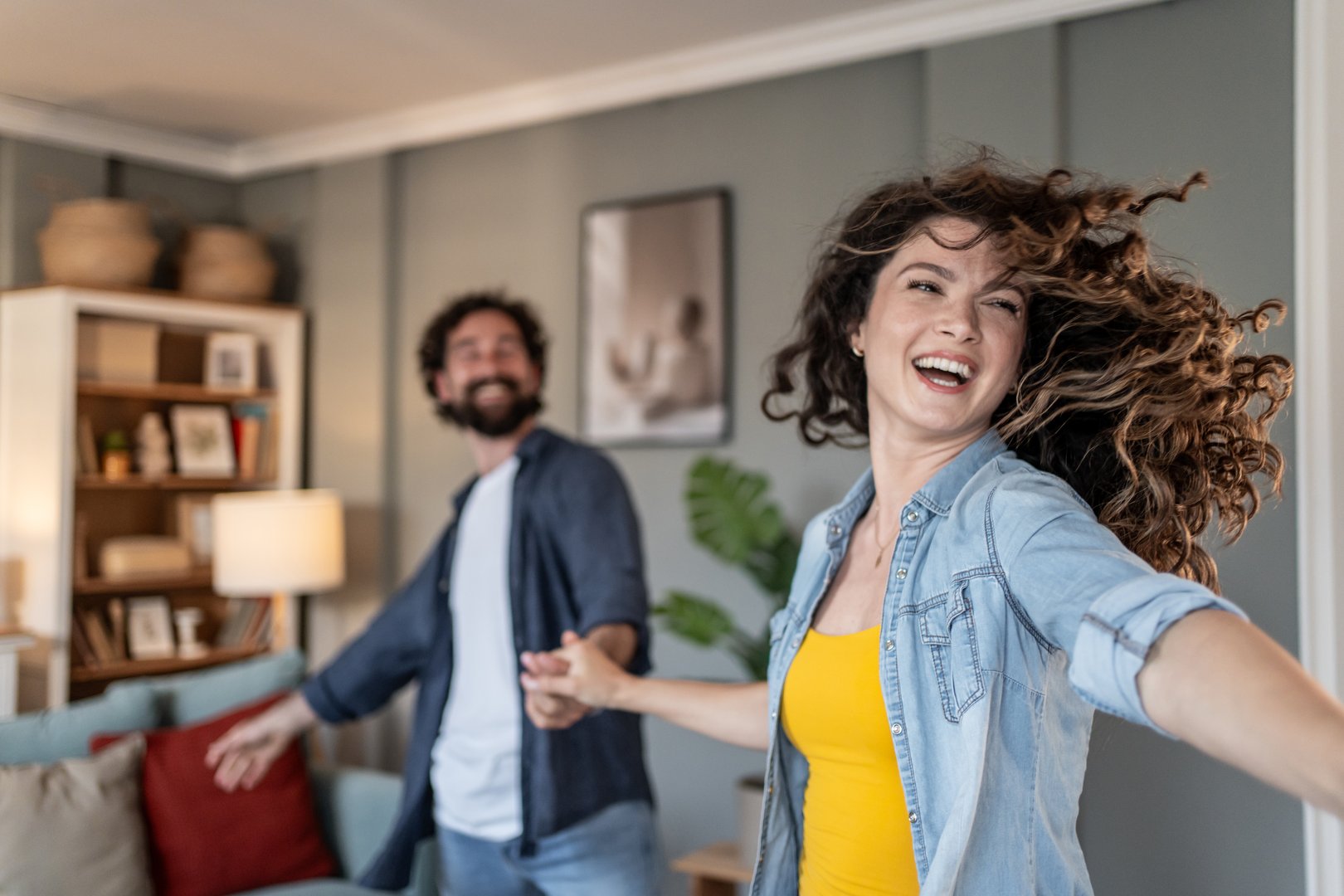 Carefree young couple is having fun while dancing together in their cozy living room, enjoying their time together and celebrating their love and happiness