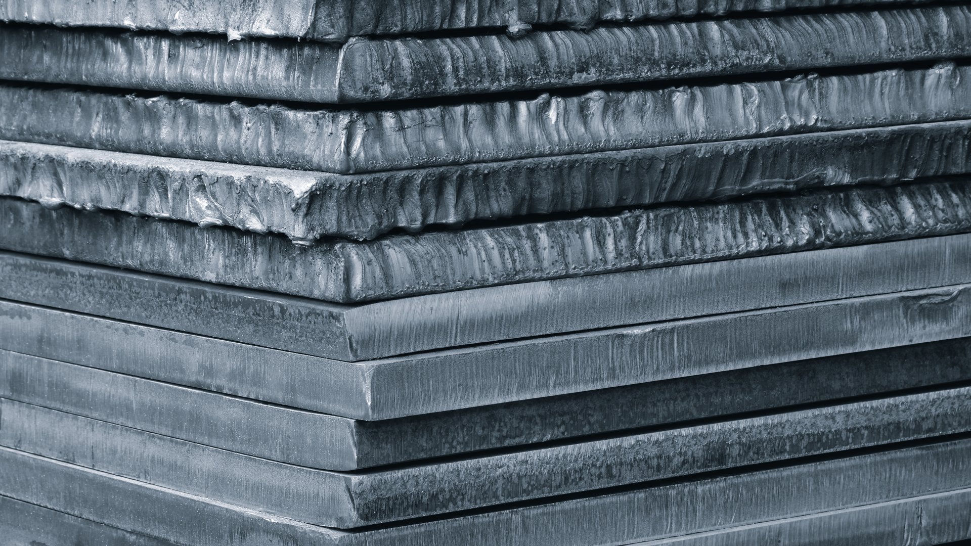 Stack of dark blue thick heavy metal plates rusty uneven surface after laser cutting. plates stacked top each other, creating sense depth and texture. scene is somewhat dark industrial  blue background