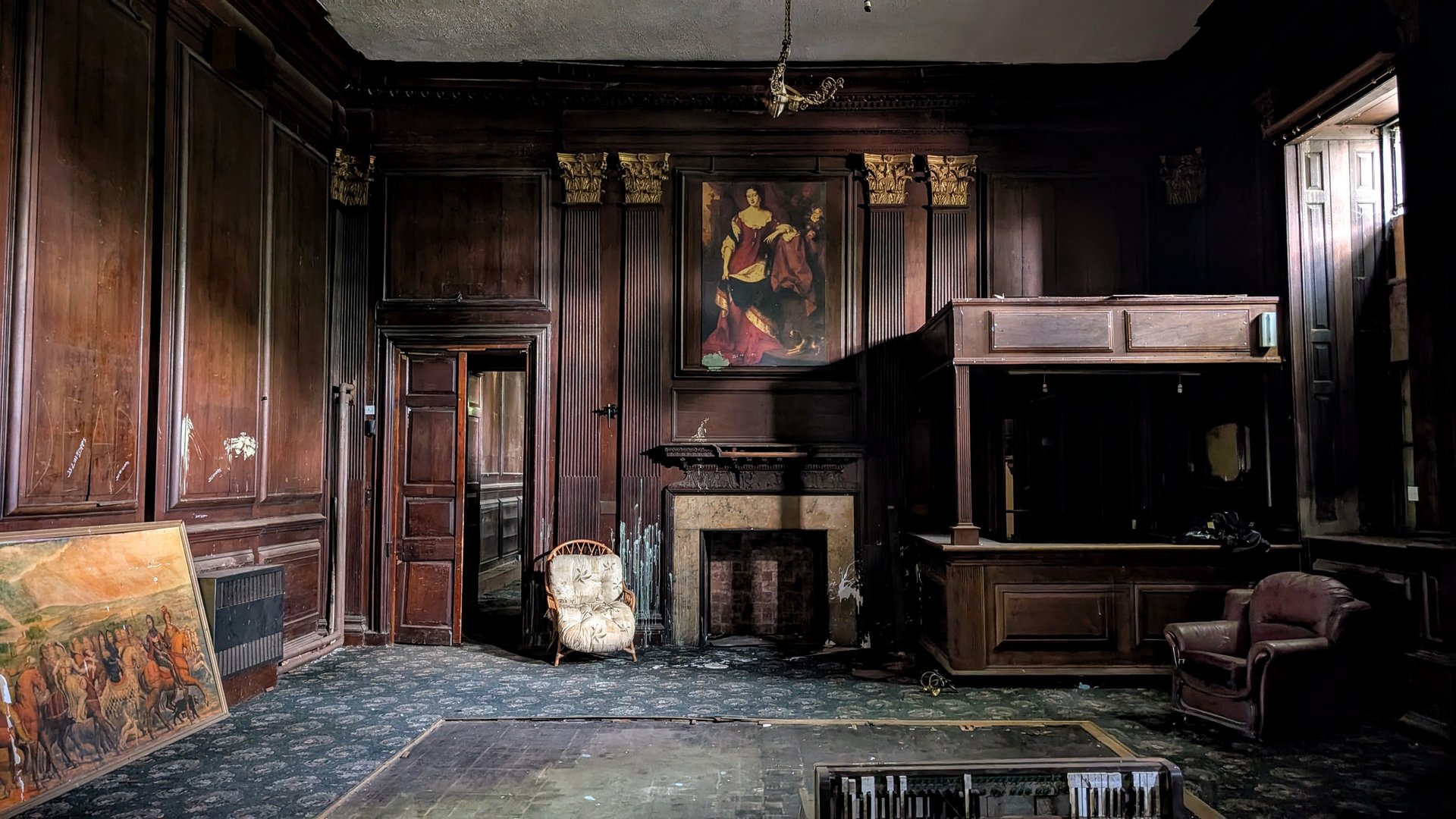 Abandoned stately home country mansion, eerie interior living room in disrepair. Listed building with wooden walls and old fashioned armchairs from bygone era. Derelict Woolton Hall in Liverpool, historical uninhabited spooky residential place falling apart. Dilapidated wood panelling wainscoting seem apocalyptic with dark creepy shadows. Boarded up windows cast daylight for desolate vision of shadowy darkness. Decay of indoor place with medieval art over fireplace.