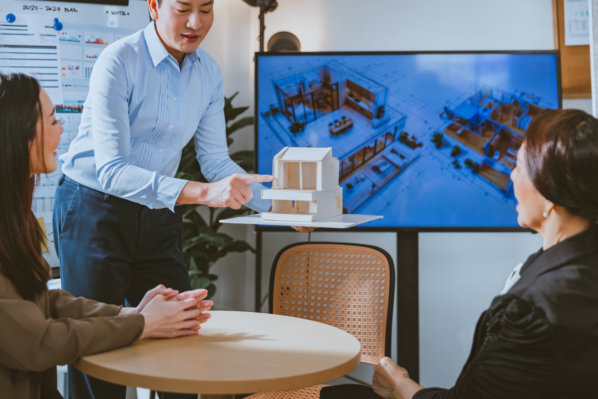 Happy young gay and senior woman professional asian architecture team in Smart Casual Clothes planning discussion and brainstorm a new business project with house model in office, teamwork meeting concept