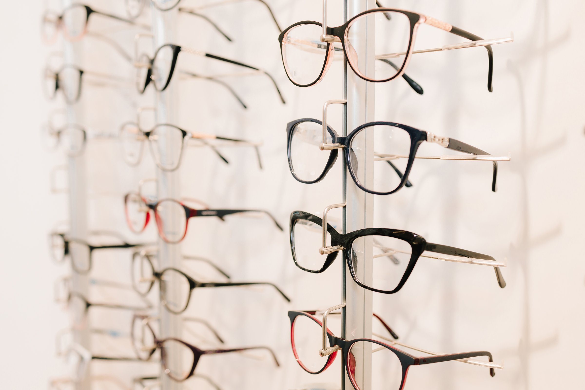 Customer chooses eyeglasses with clear lenses from the shelf. Eyesight correction. Stand of eyeglasses with different frames in the optical store