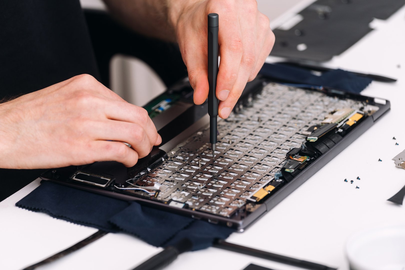 Man is sitting at a desk, focused on repairing laptop with tools and parts scattered around him. Warranty service, replacement of a broken element in computer. Repairman replace keyboard in notebook