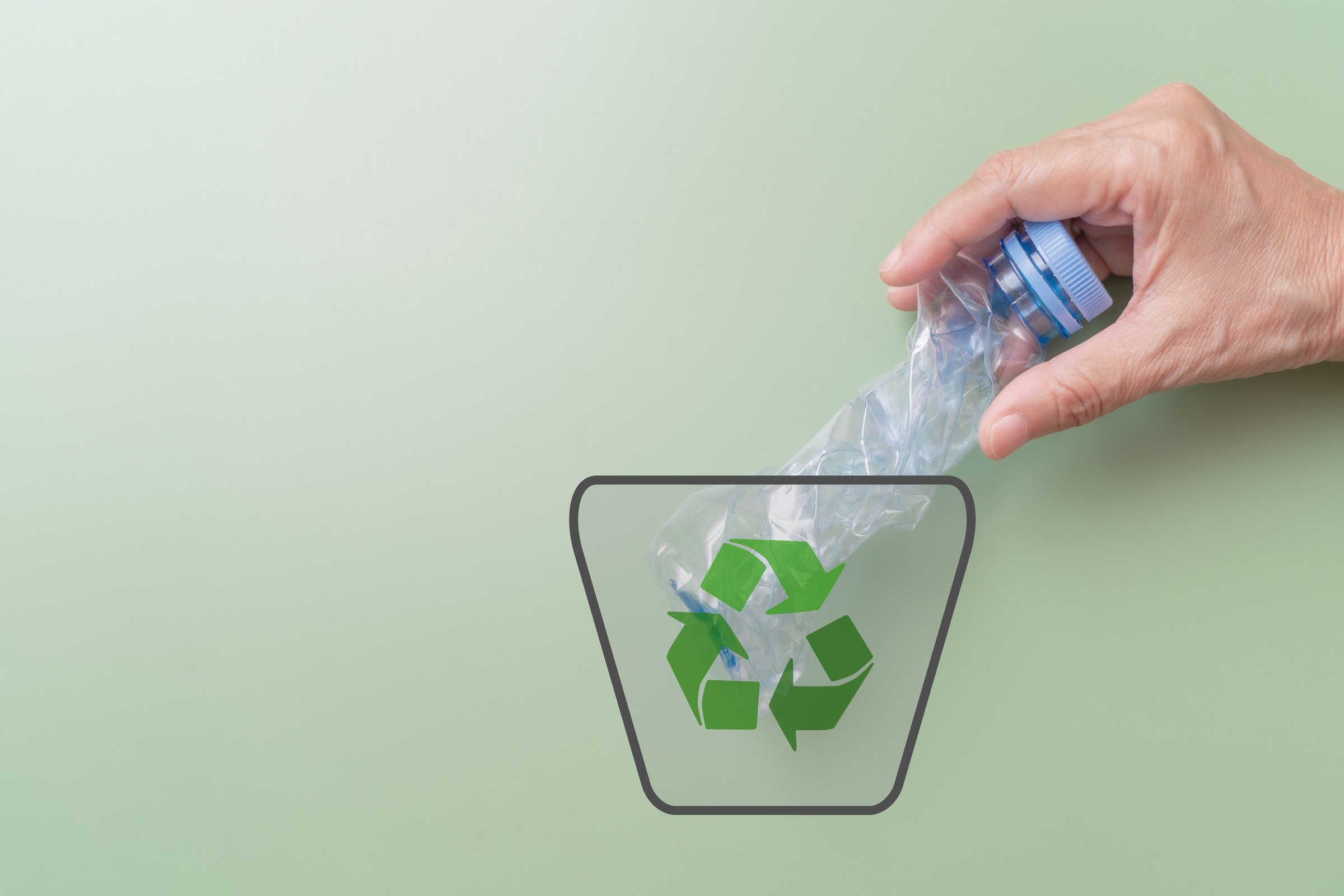 hand throws transparent plastic bottle package in bin with recycle sign on green background