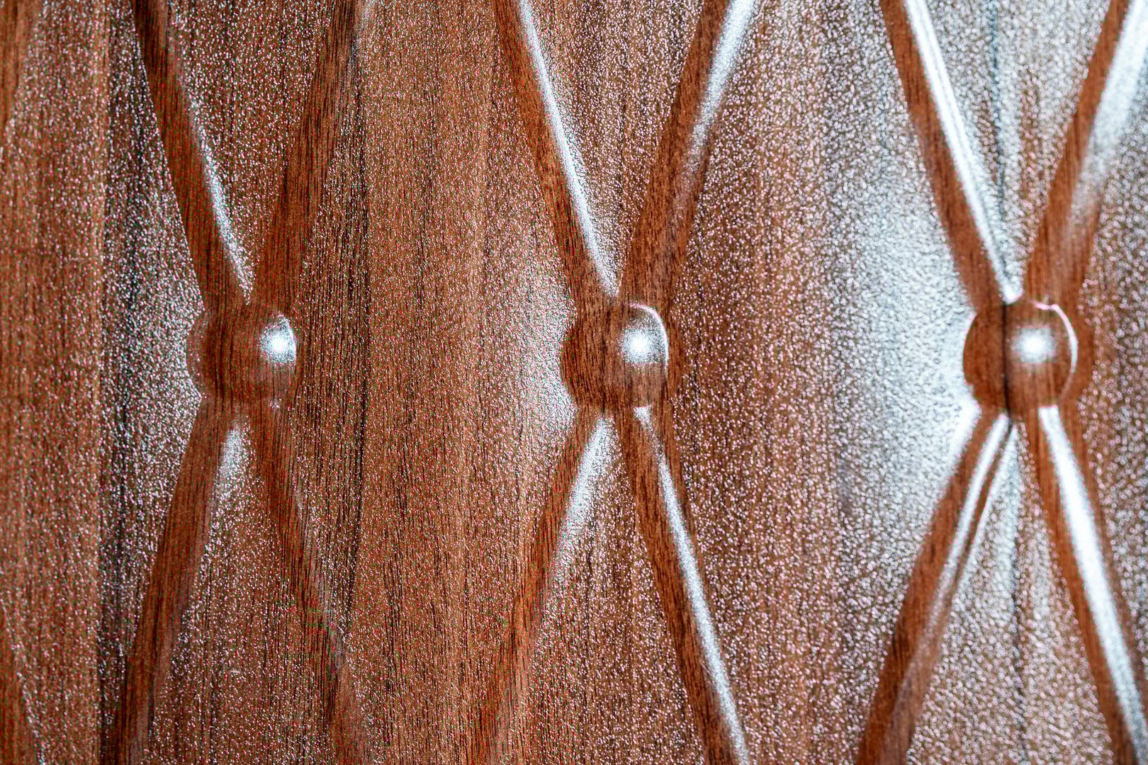 Close-up of polished wood panel featuring a carved diamond pattern and button-like accents