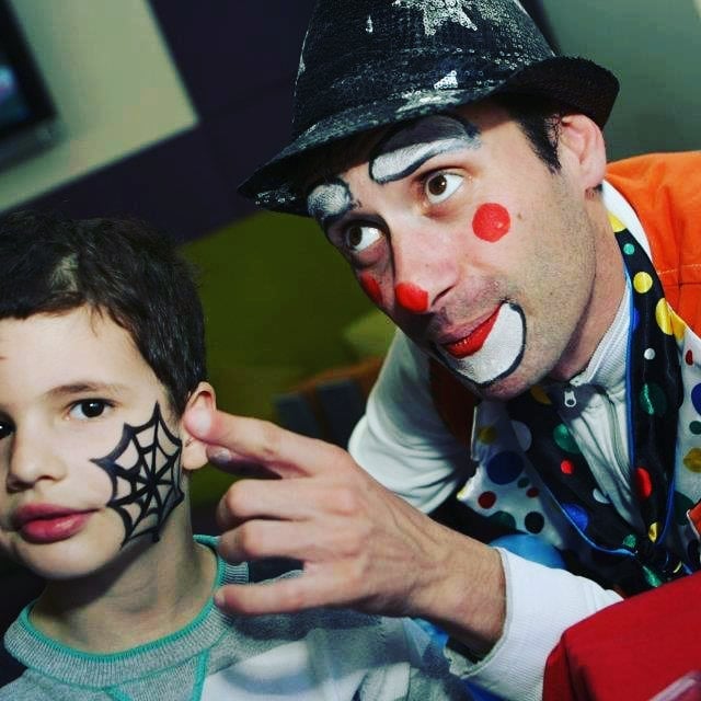 Child with face painted as a spiderweb and a clown with face paint and a polka-dot outfit in a playful pose.