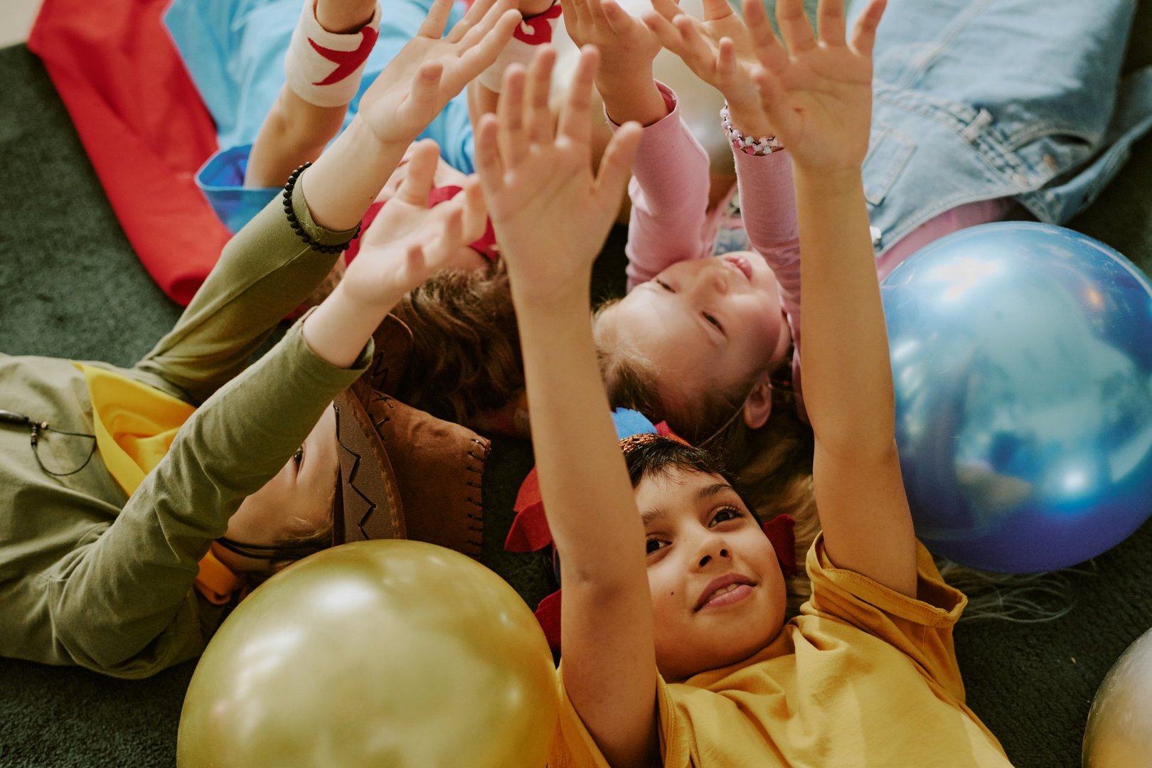 Group of multiethnic children lying on floor reaching hands upward