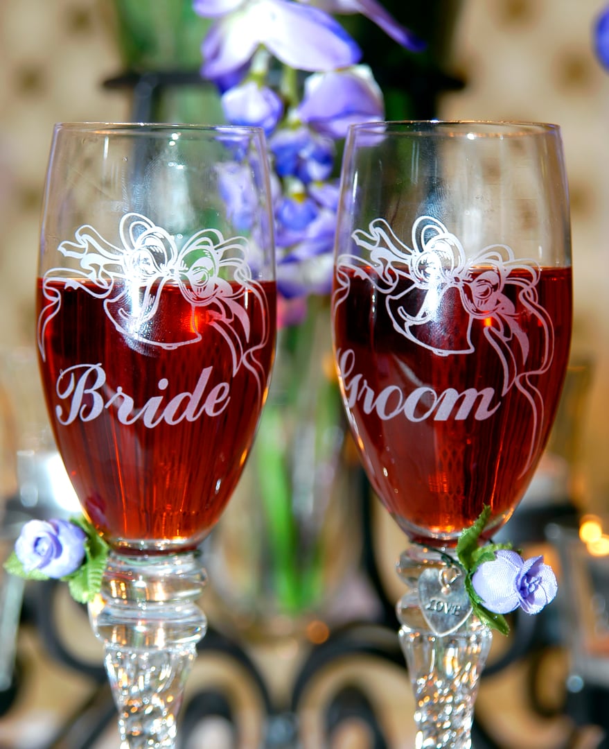 His and her champagne glasses sit side by side at wedding reception venue.  One has "His" on it and the other has "Her" on it.