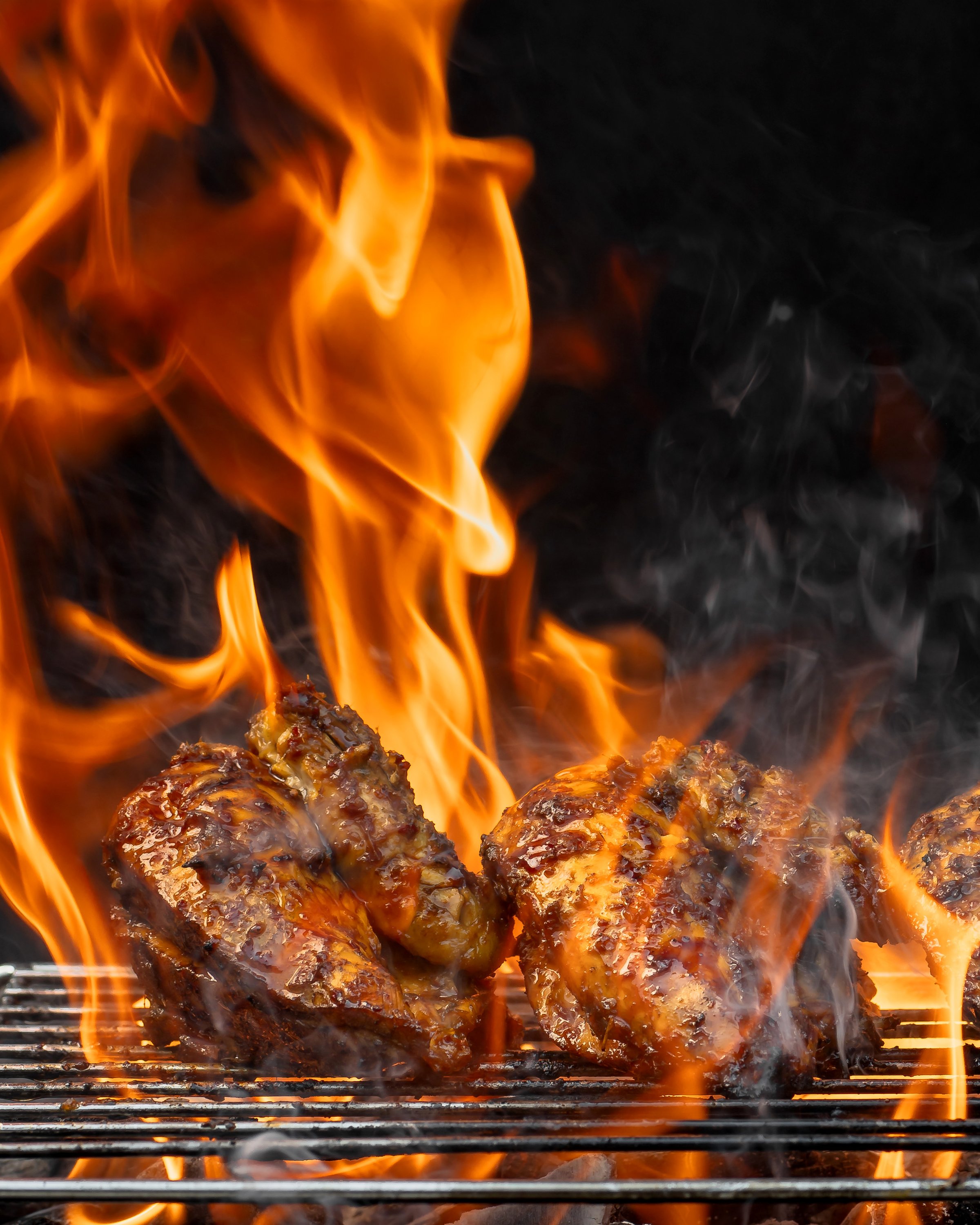 Two pieces of chicken are cooking on a grill, with flames and smoke surrounding them. Concept of excitement and anticipation for a delicious meal
