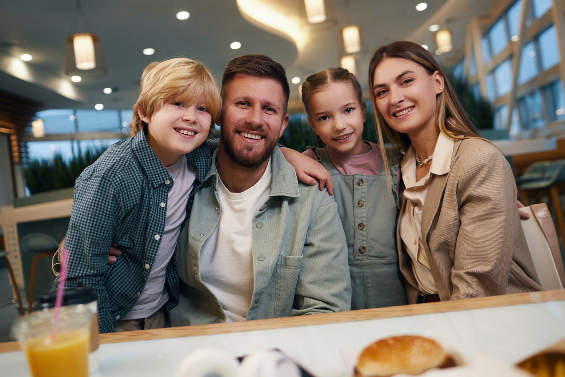 Dutch angle shot of Caucasian young family sitting at table in food court and posing for portrait