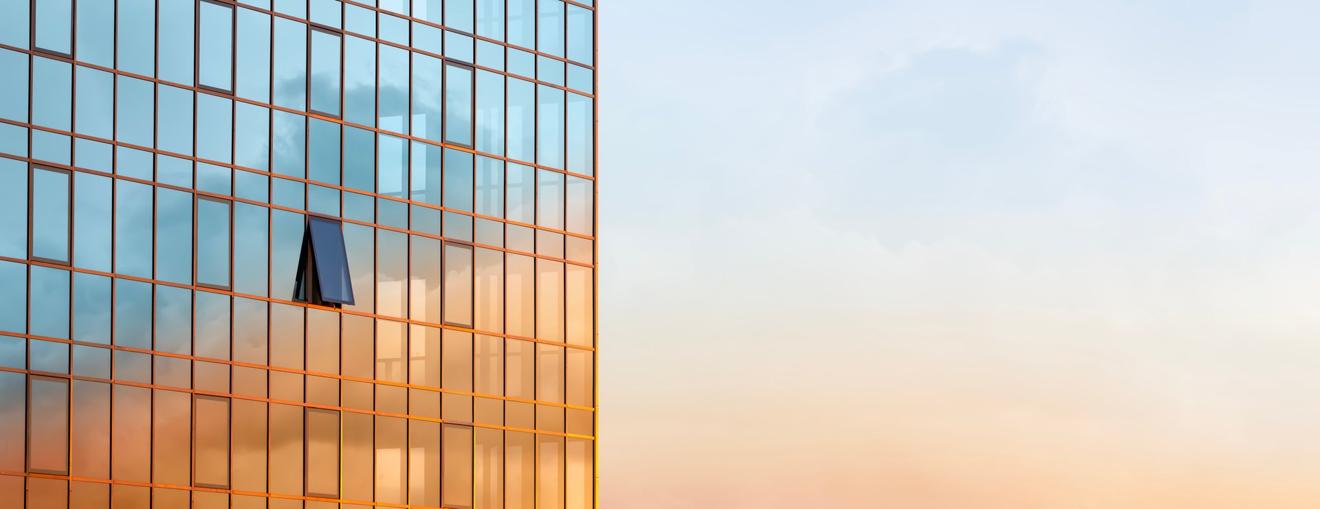 The glass wall of a modern building against the sky with the reflection of clouds on it during a golden sunset. Copy space