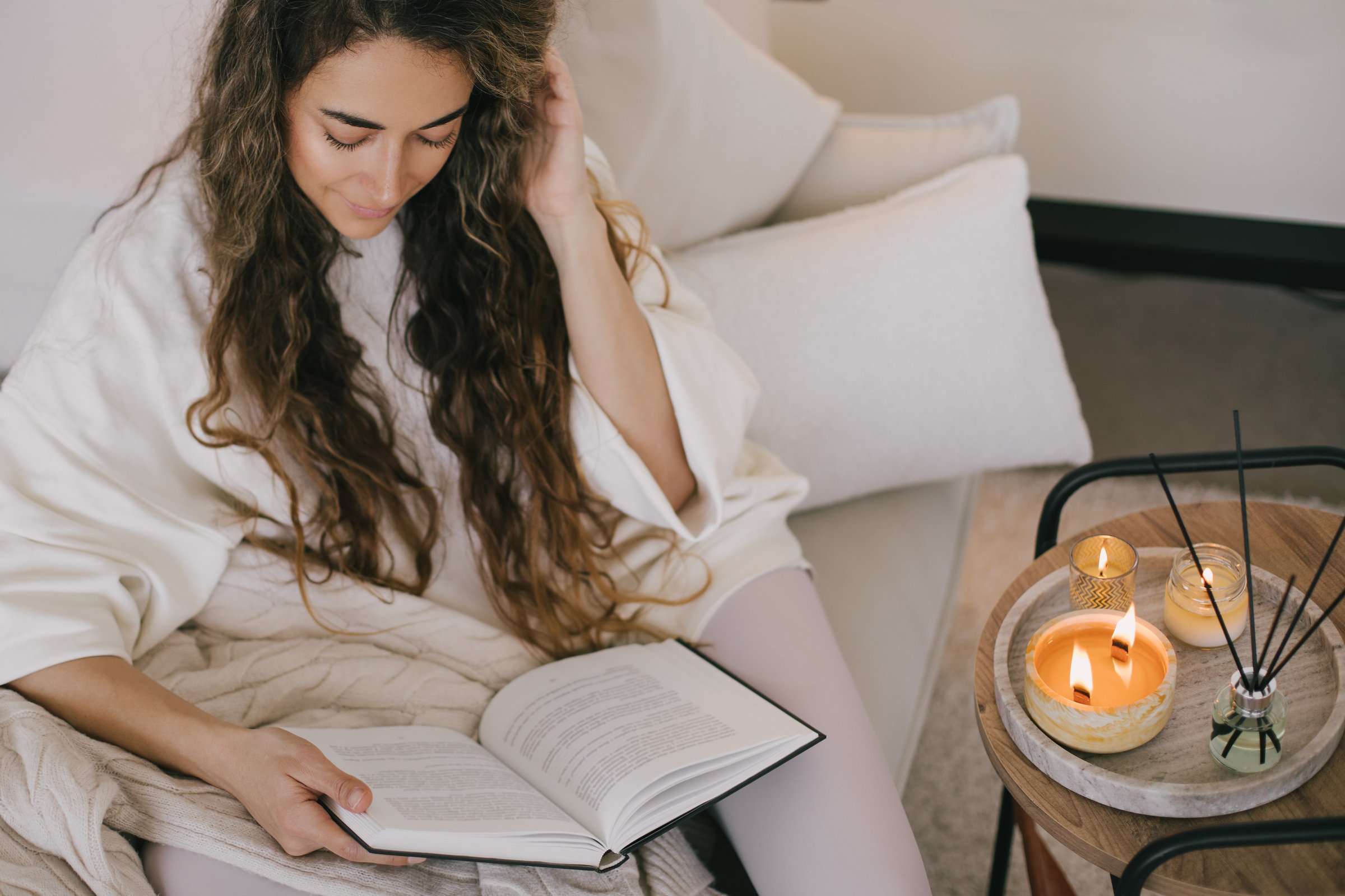 Young woman reading book and drinking tea, relaxing on sofa in a cozy living room