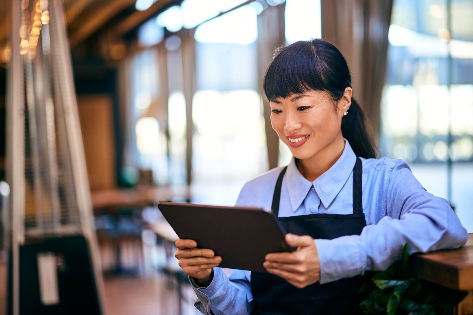 Asian woman working as a waitress, dressed in a uniform, using a digital tablet.