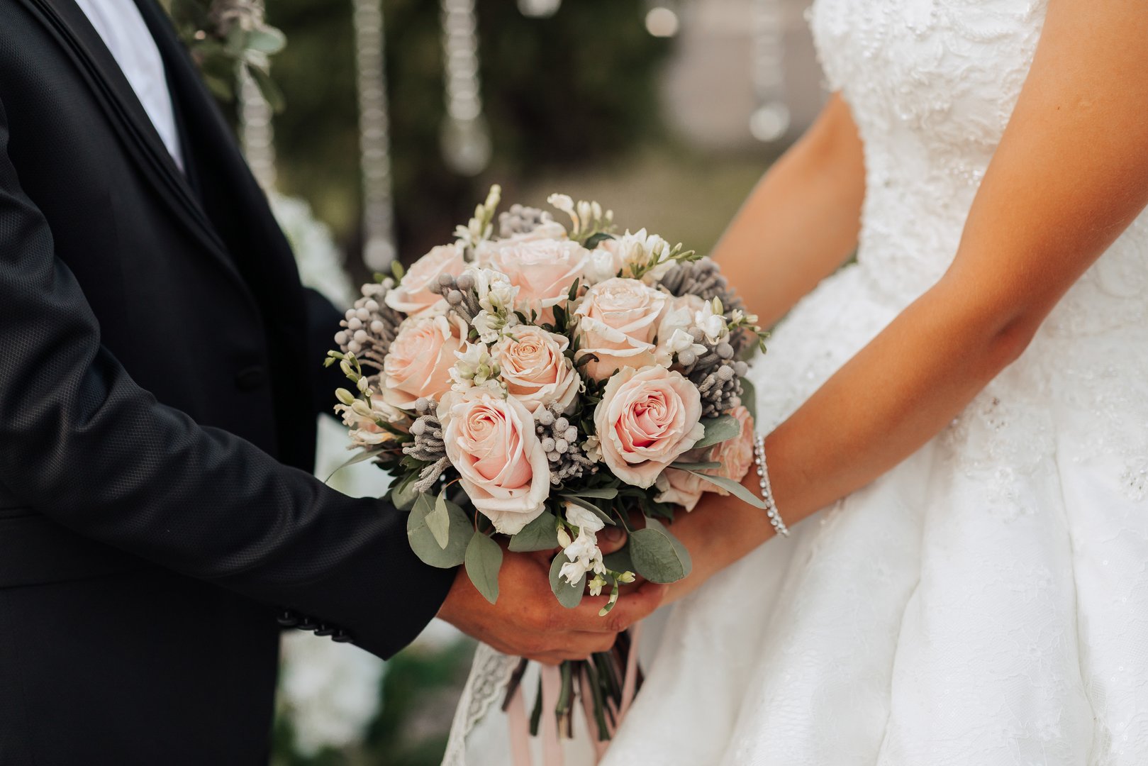 A man and woman are holding a bouquet of flowers. The man is wearing a suit and tie, and the woman is wearing a wedding dress. The flowers are pink and white, and they are arranged in a vase